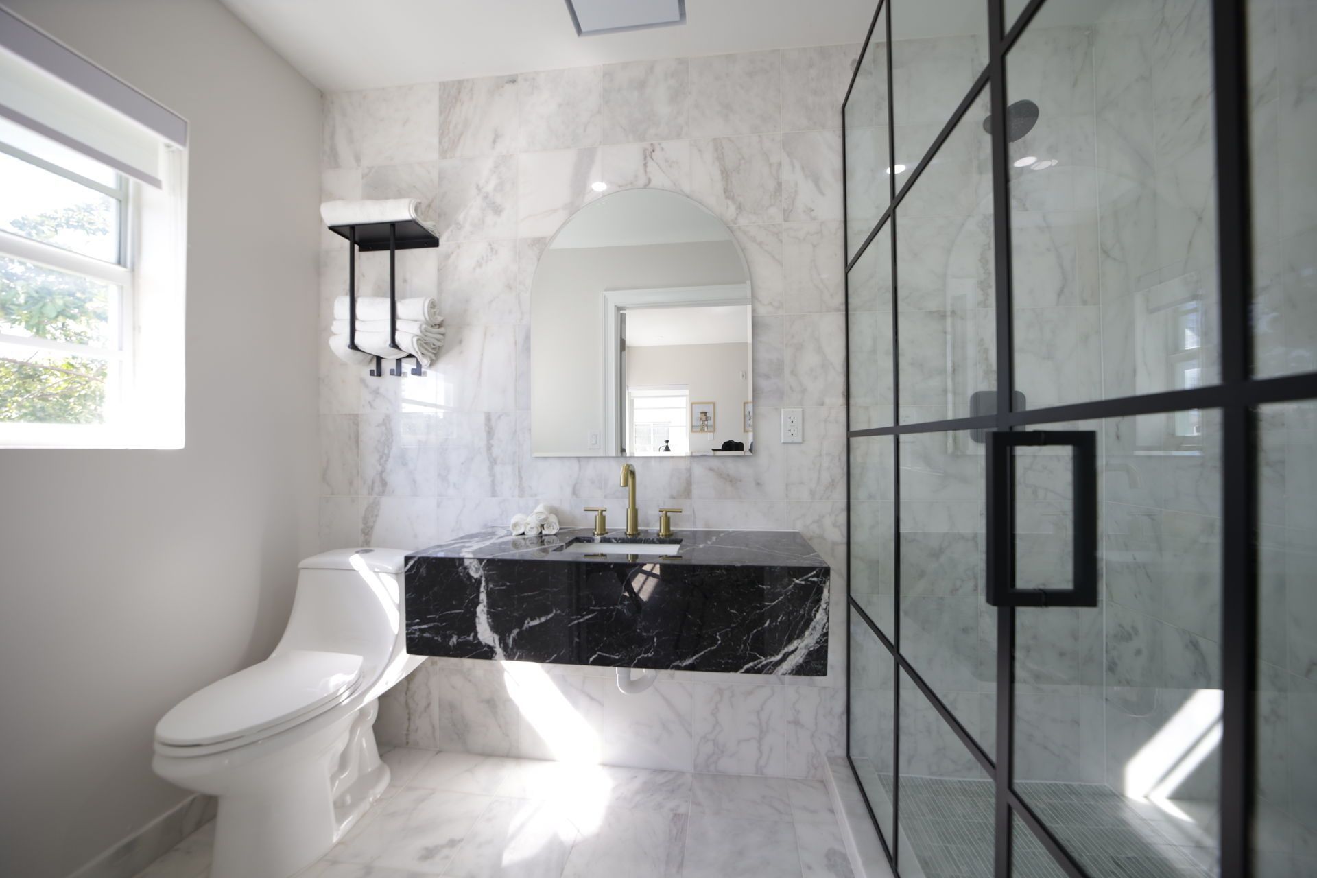 Modern bathroom with marble walls and black marble vanity. Glass shower enclosure.