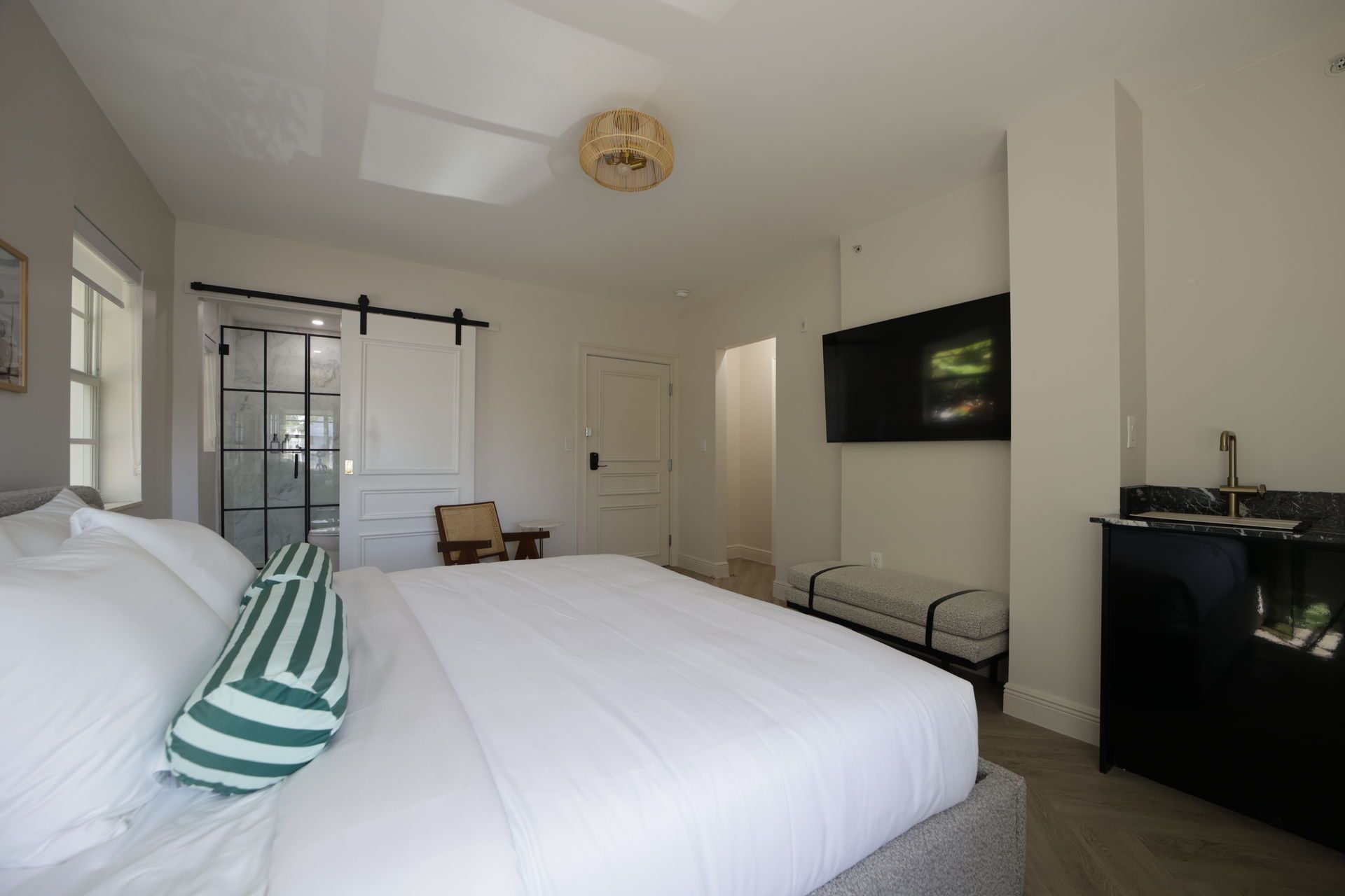 Bedroom with a large bed, TV on the wall, black cabinet with sink, and sliding glass door to a bathroom.