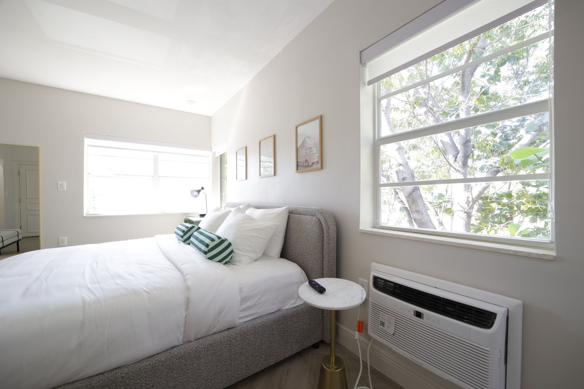 Bedroom with bed, windows, and small white side table. Bright with white and light gray walls.