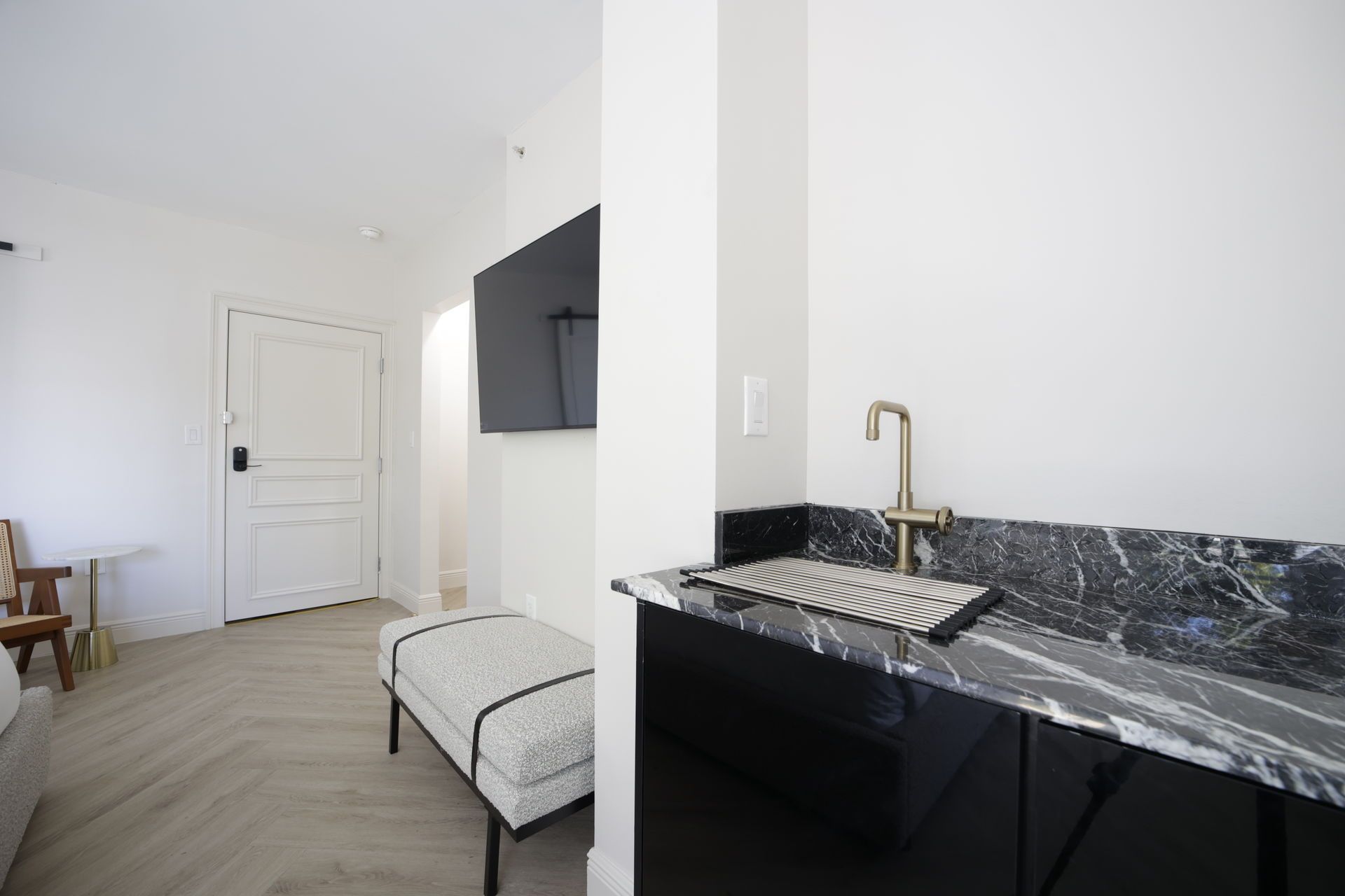 Modern room with marble countertop, black cabinets, bench, TV, and doorway.