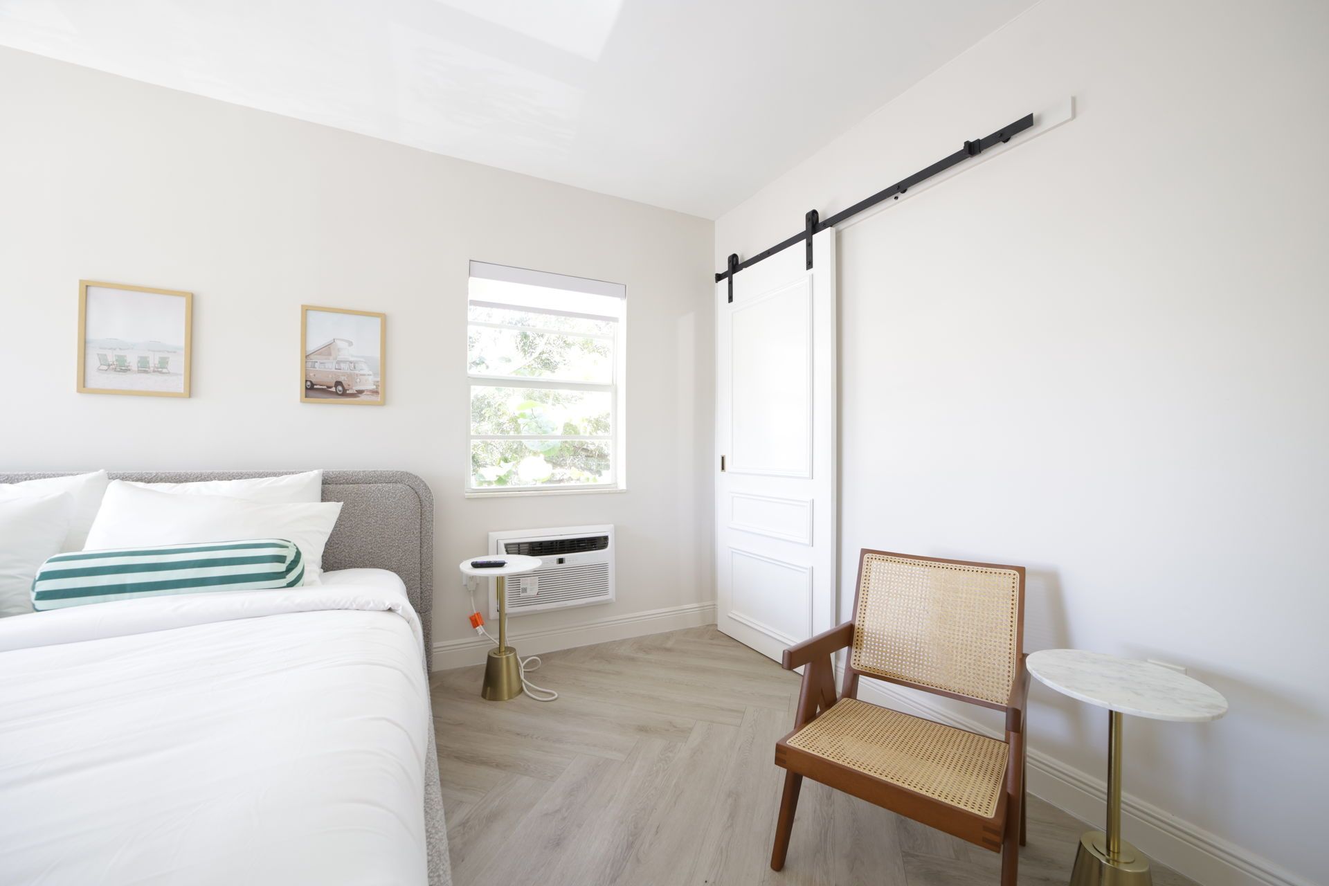 Bedroom with white walls, sliding door, window, bed, chair, and small tables.