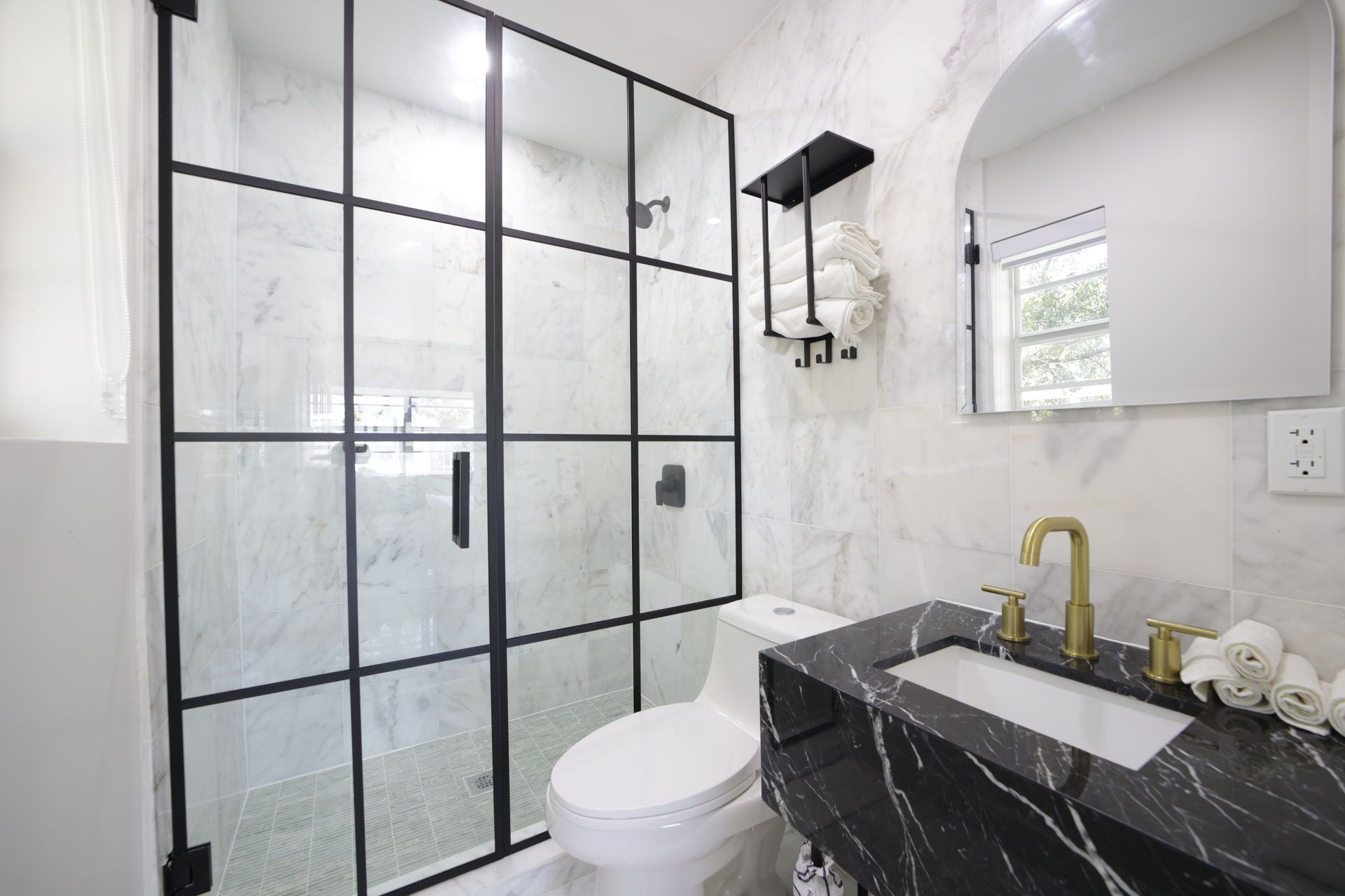 Bathroom with black-framed shower, marble walls, black vanity, gold faucet, and a large mirror.