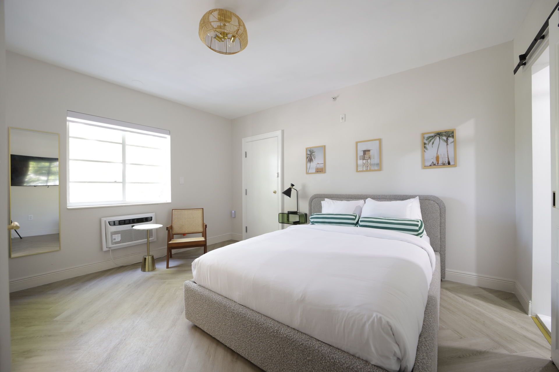 Bedroom with a bed, small side table, and wall art. White walls, wood floor, and natural light.