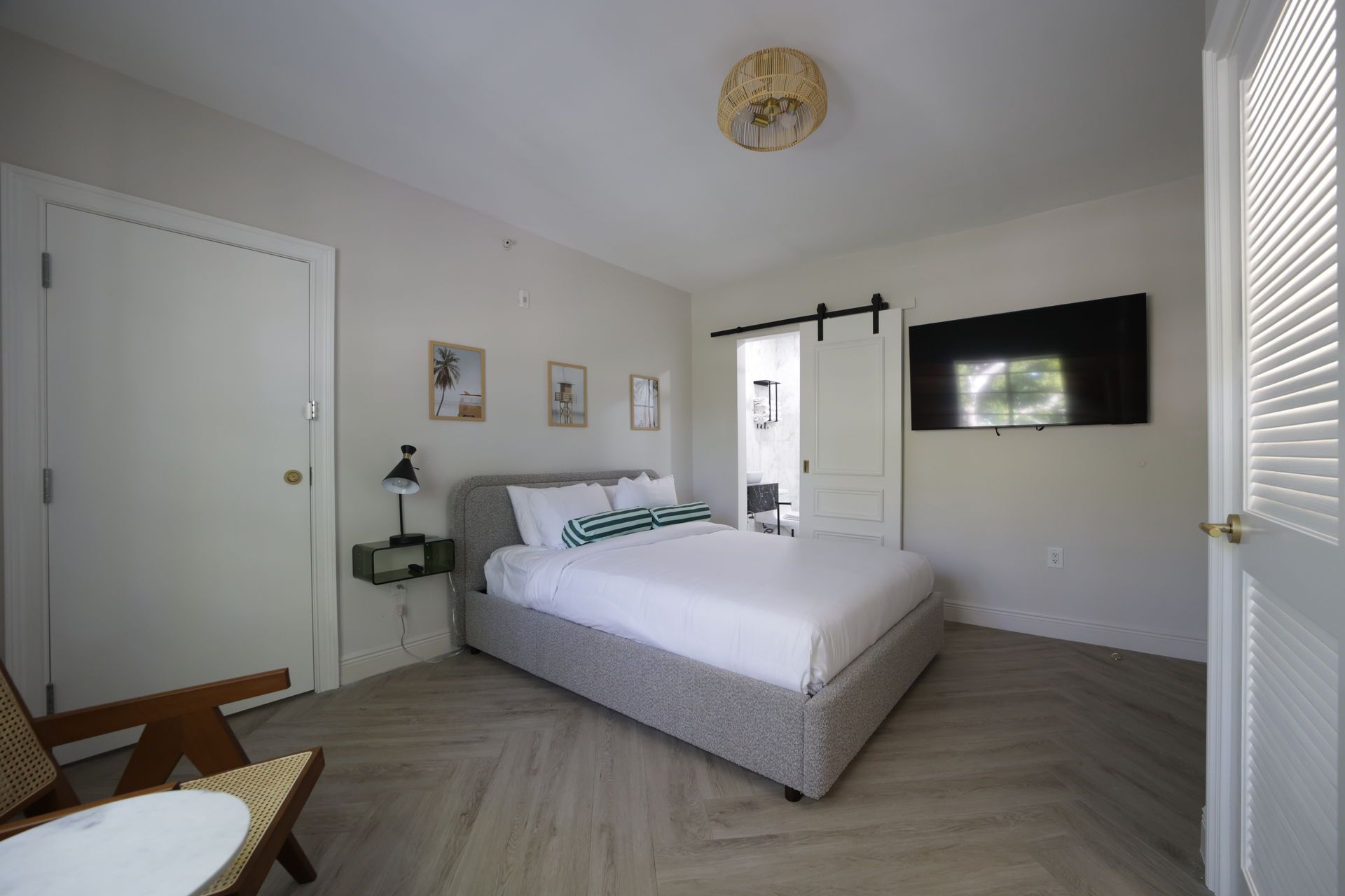 Bedroom with a bed, TV, and open doorway, featuring light walls and wood floors.