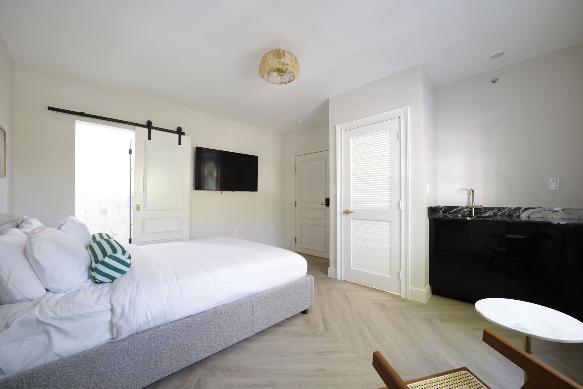 Bedroom with bed, television, open door, and mini-bar. Light wood floors, white walls.