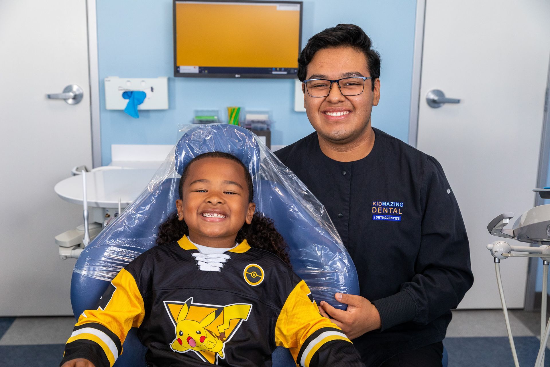 Smiling child in a dental chair with a dentist in a black shirt, in a clinic room