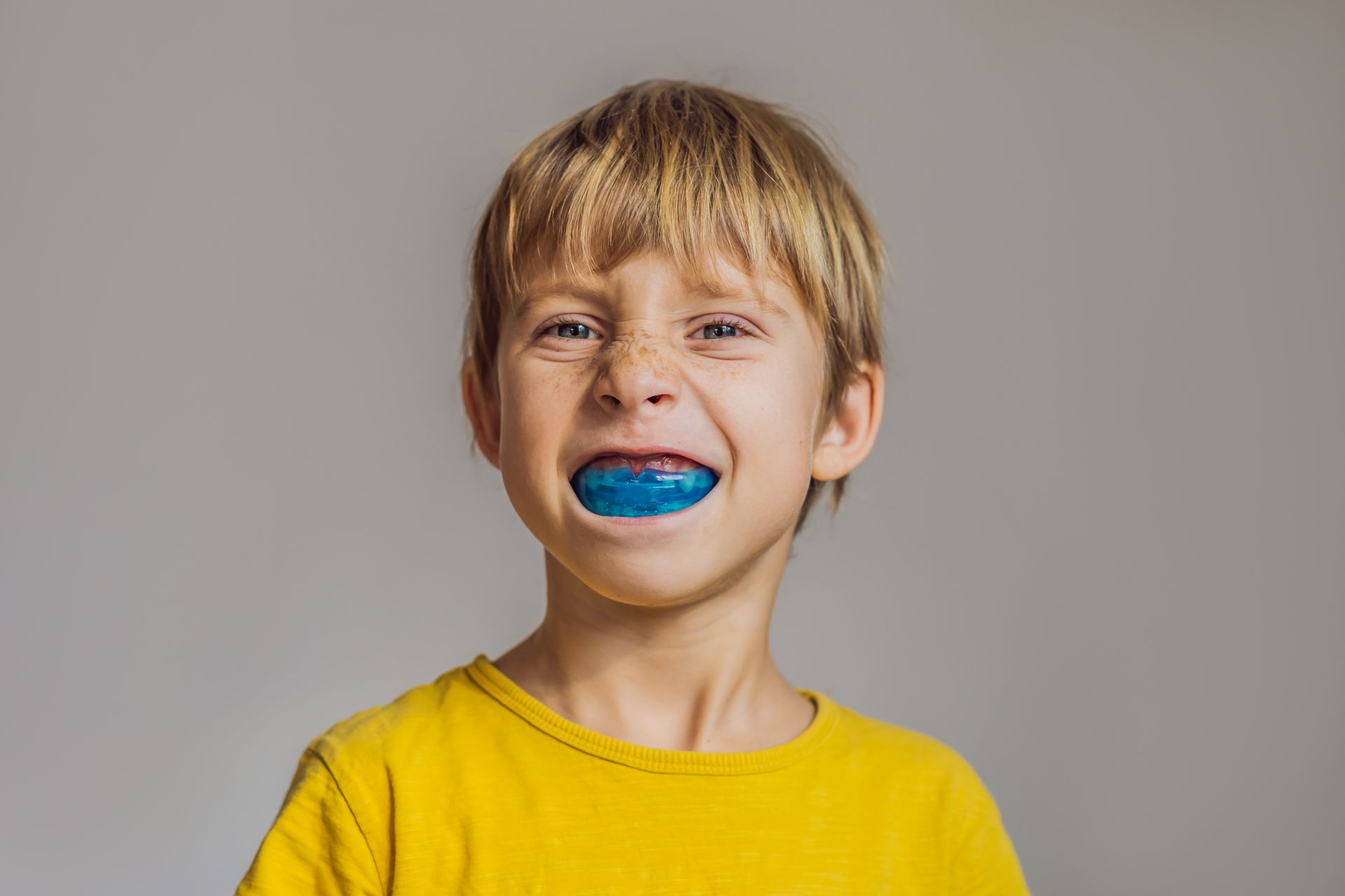 Smiling child with blue mouth paint and a yellow shirt against a plain gray background