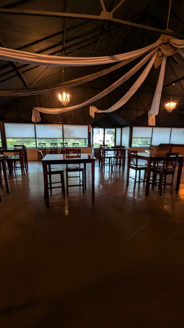 Empty rustic dining area with wooden tables, draped ceiling fabric, and warm hanging lights.