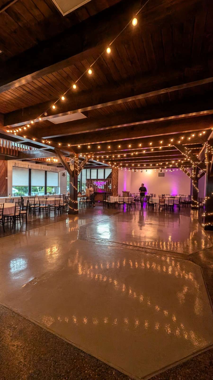 Rustic indoor event hall with string lights, polished dance floor, and tables set for a gathering