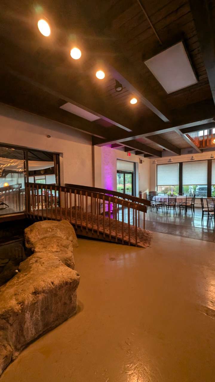 Empty modern restaurant interior with wooden bridge, stone feature, warm lighting, and large windows