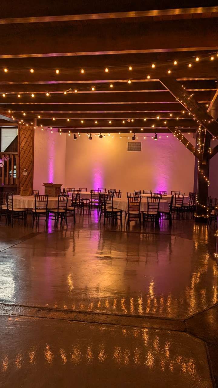 Empty indoor event space with string lights, wooden beams, and purple ambient lighting reflected on the floor