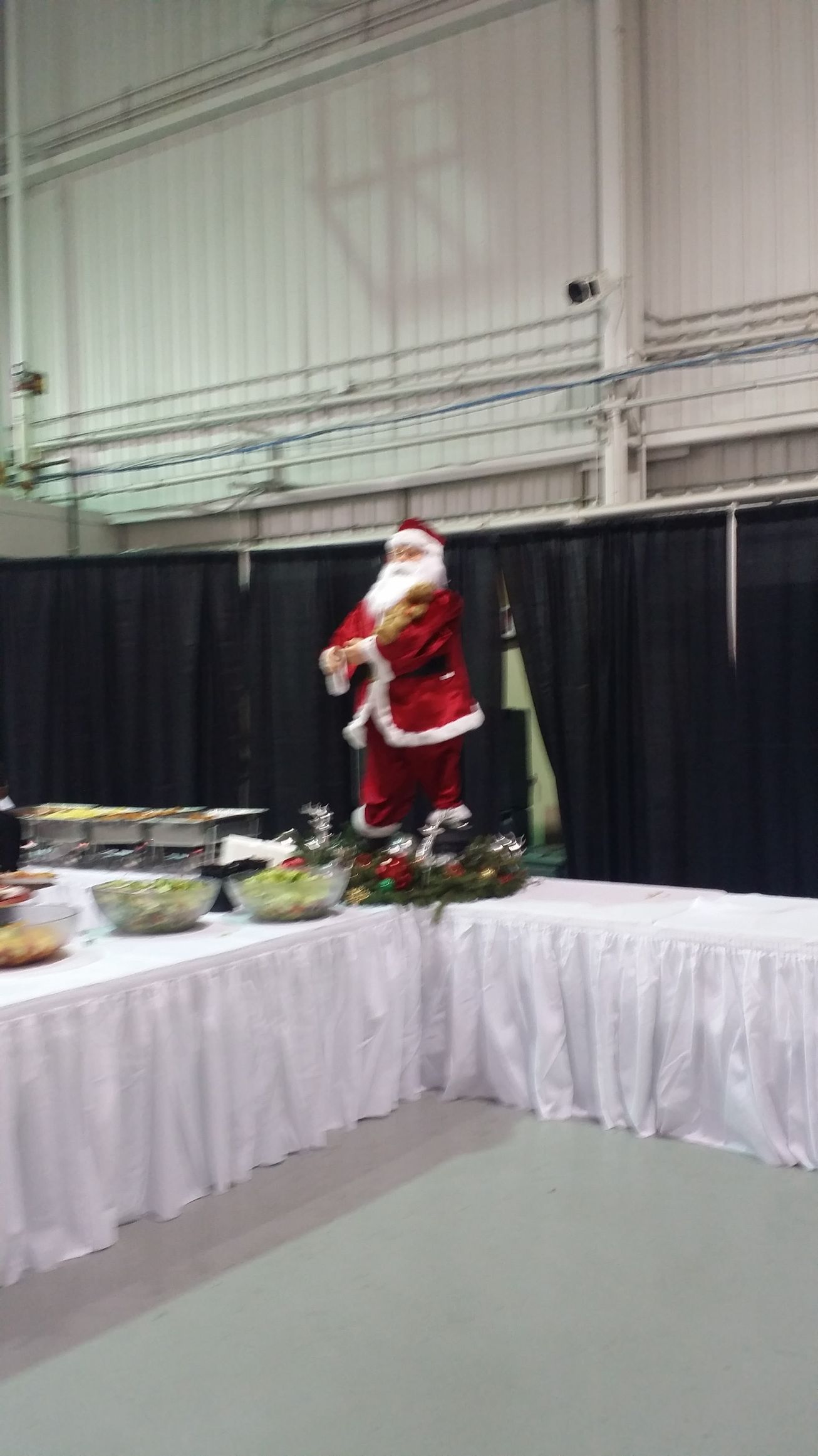 Santa figurine on a banquet table at an indoor event, with black drapes and white walls in the background