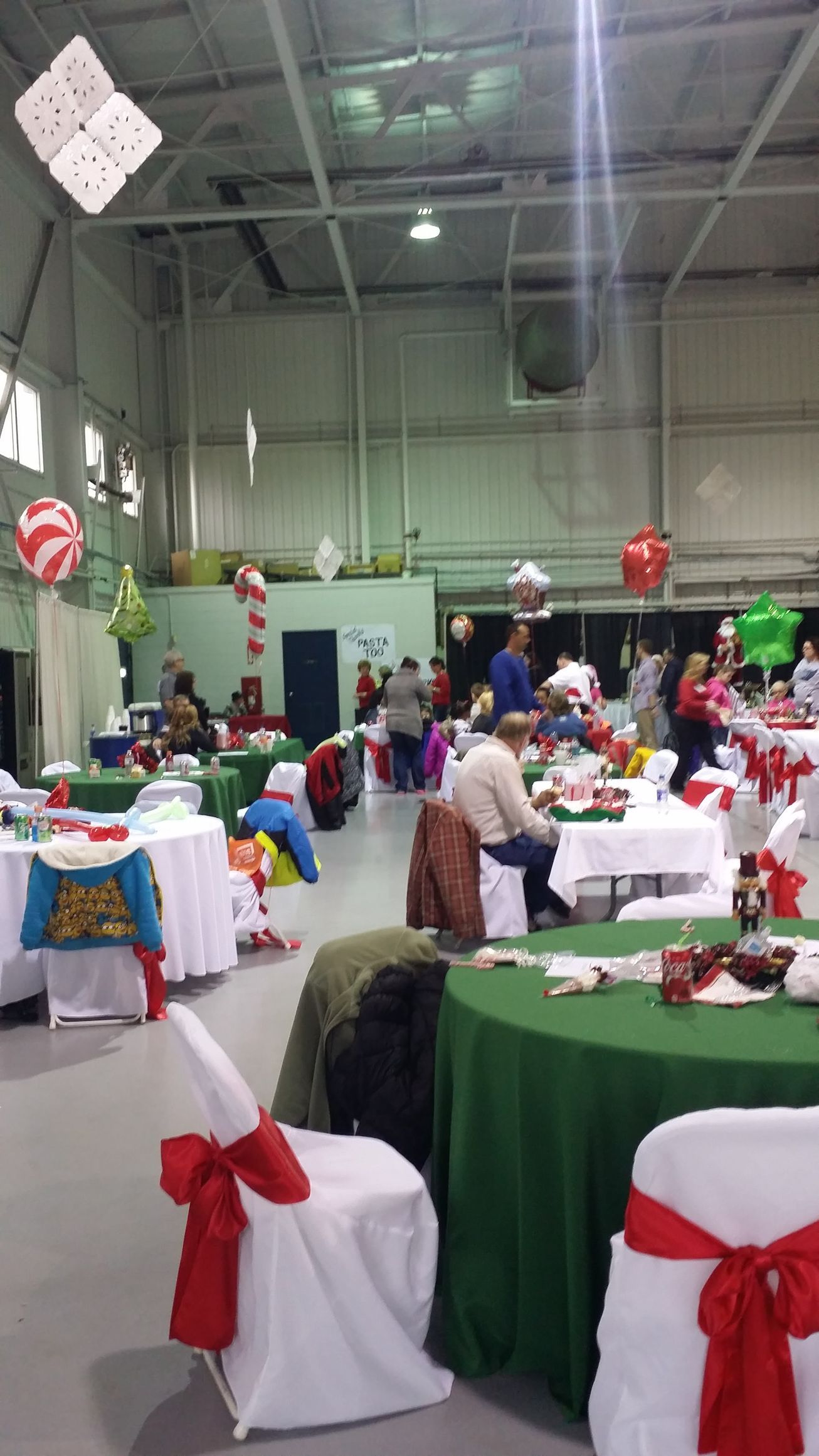 Decorated banquet hall with round tables, white chair covers and red bows, set for a festive holiday event.