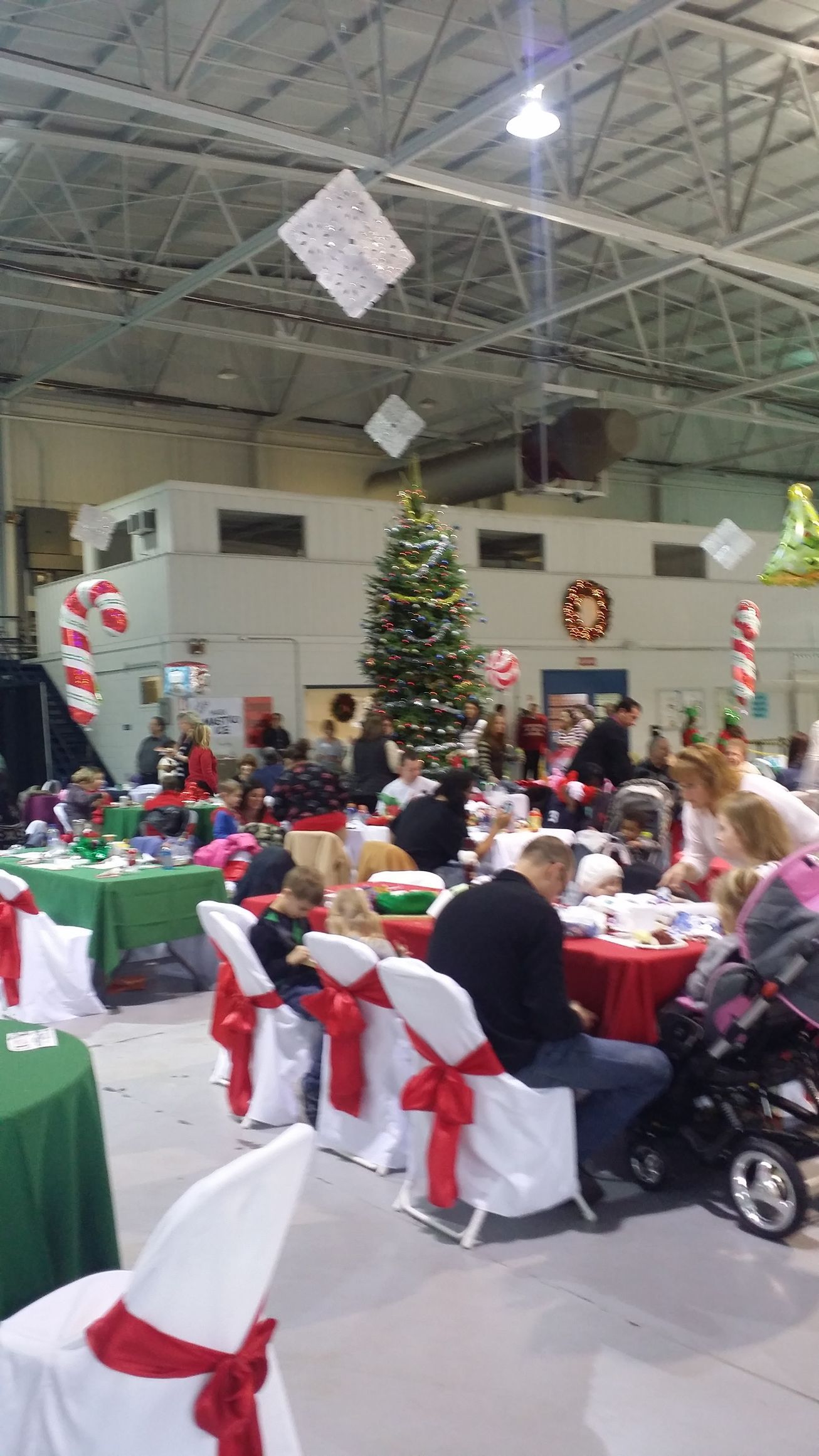 Holiday banquet in a decorated hall with tables, white chairs with red bows, and a lit Christmas tree