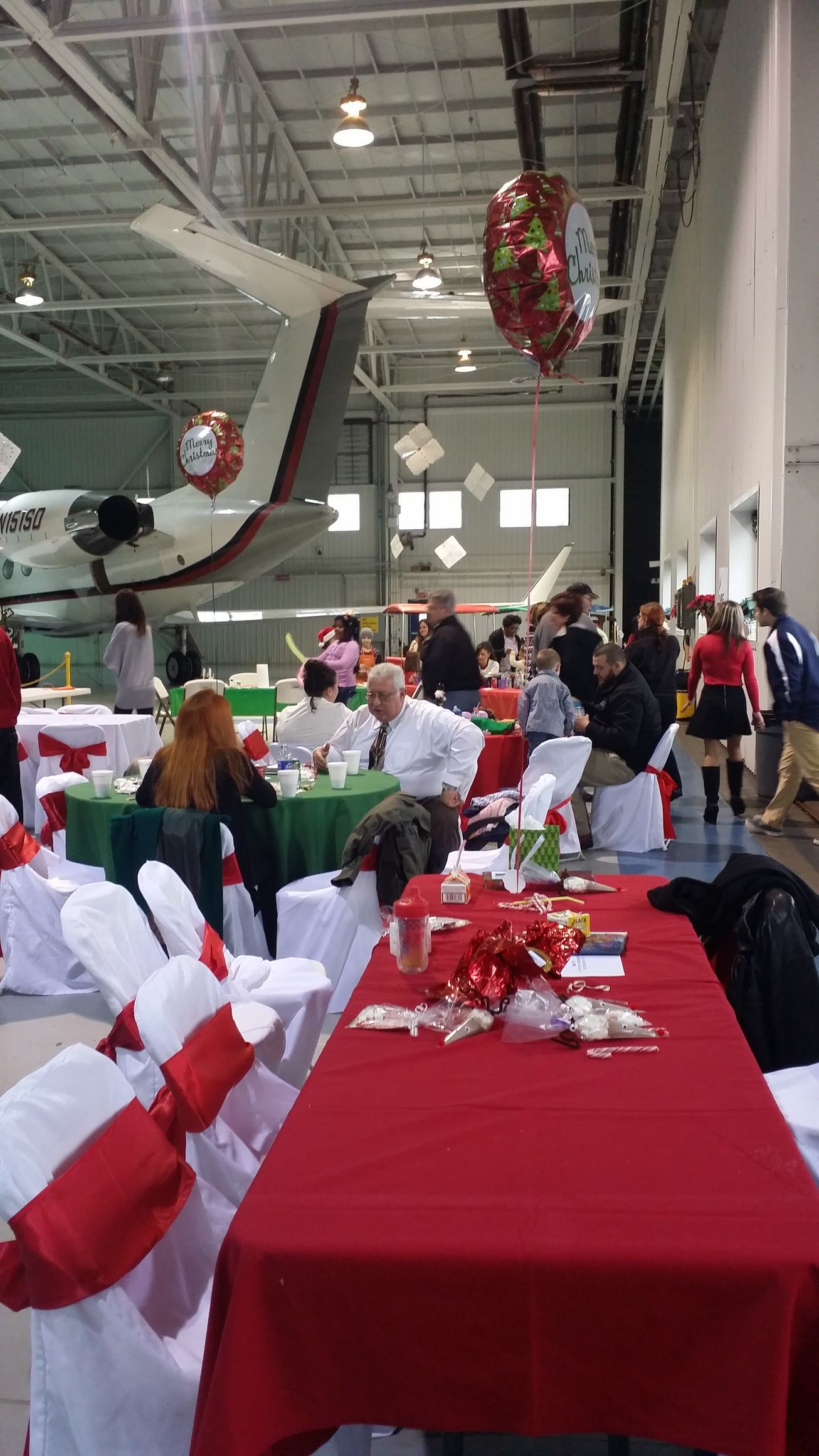 Decorated banquet table in a large hall with red tablecloths and people mingling in the background