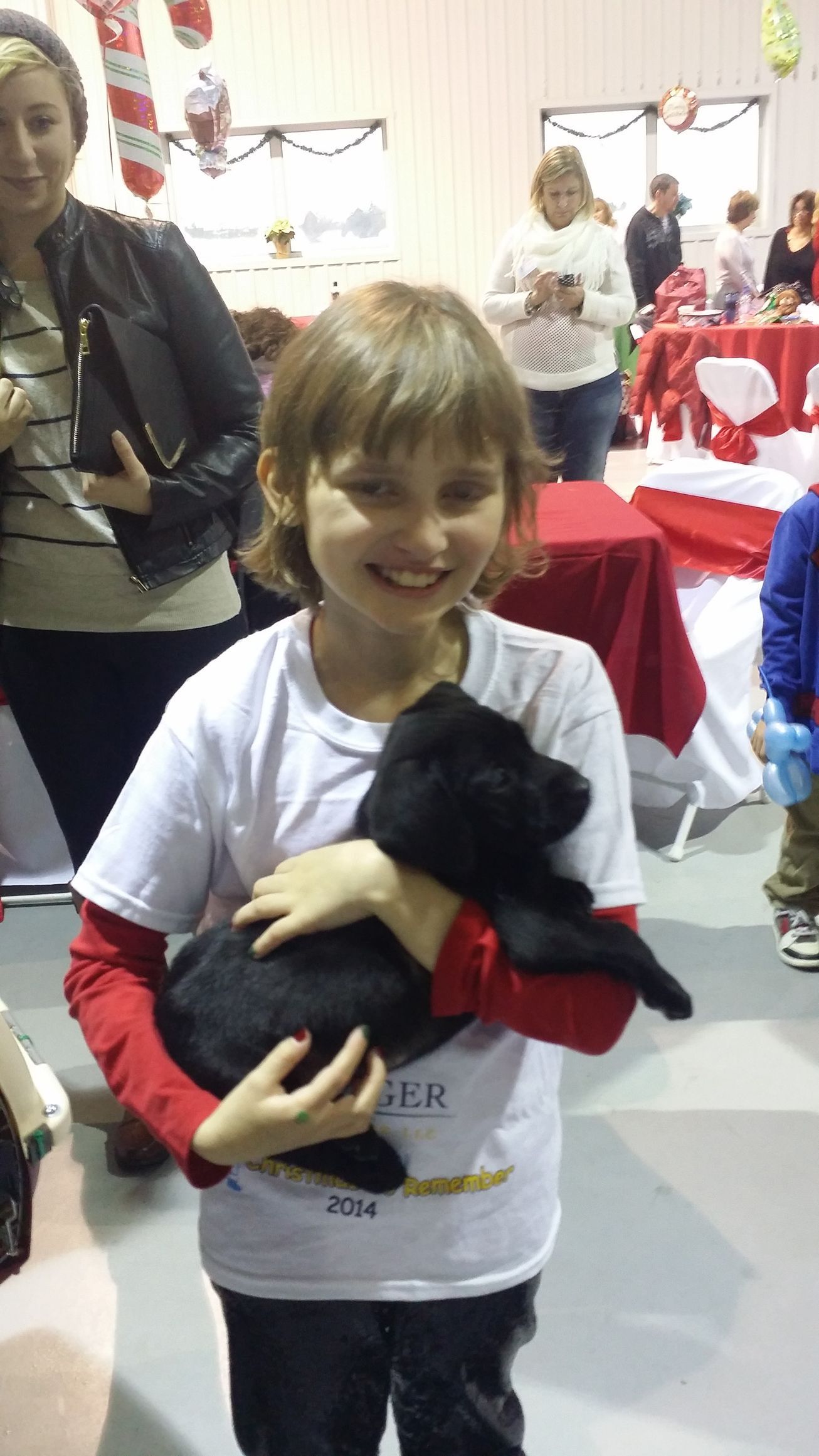 Smiling child holding a black stuffed cat at an indoor event with red tablecloths