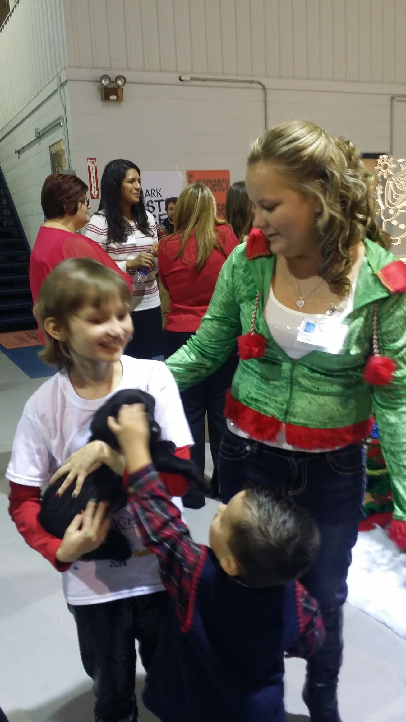 Woman in a green top with two children at an indoor event, smiling and interacting.