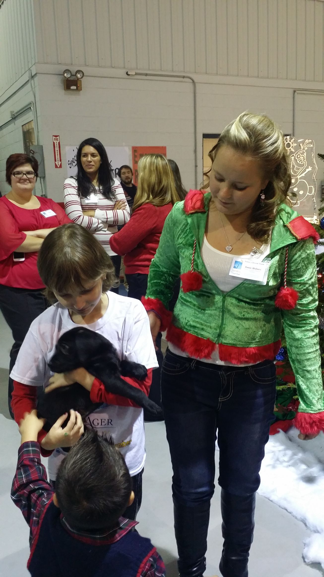 People in a room at a festive gathering, including a woman in a green-and-red top with children nearby.