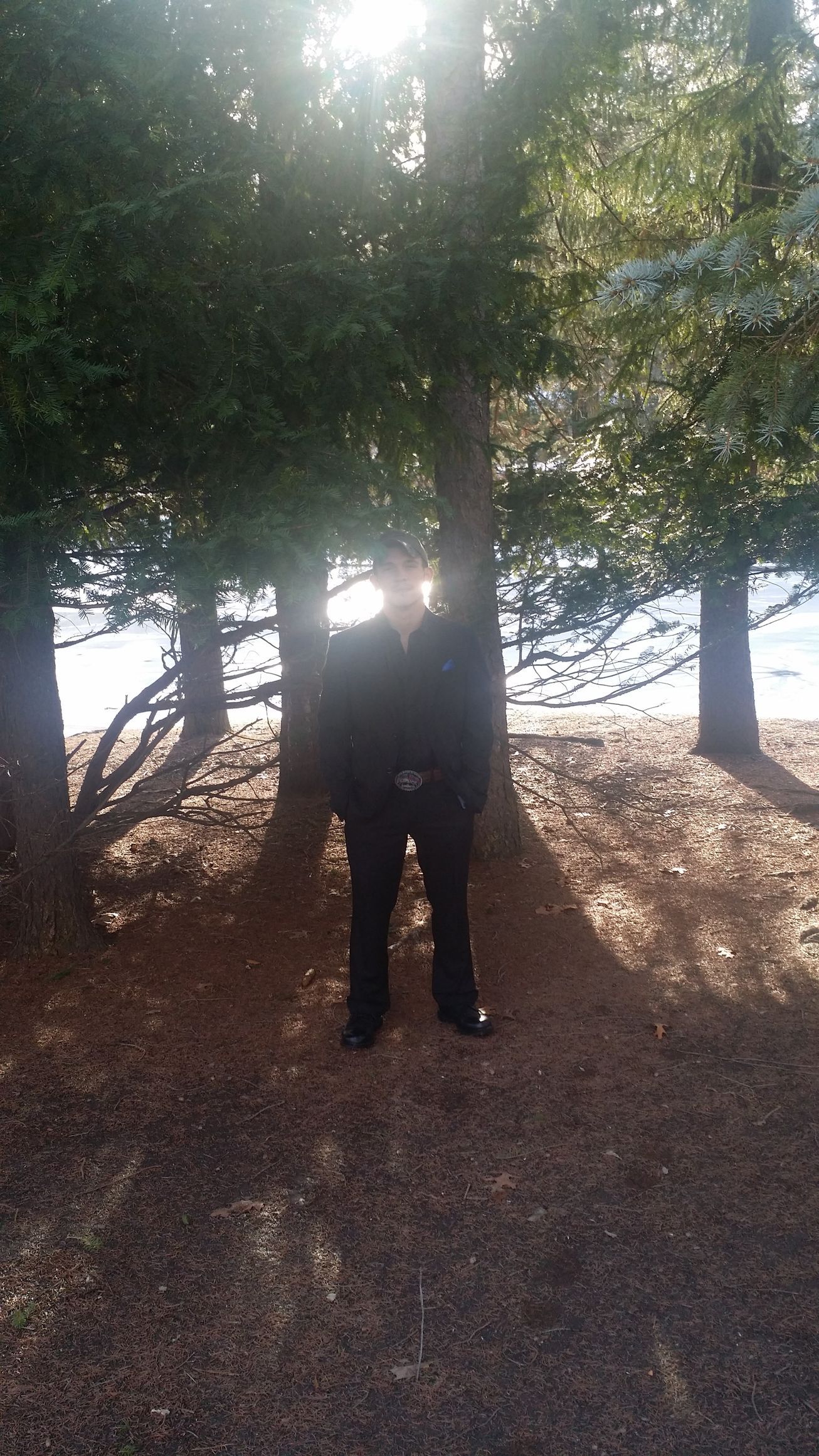 Person standing under a tree in a sunny wooded area with bright light behind them.