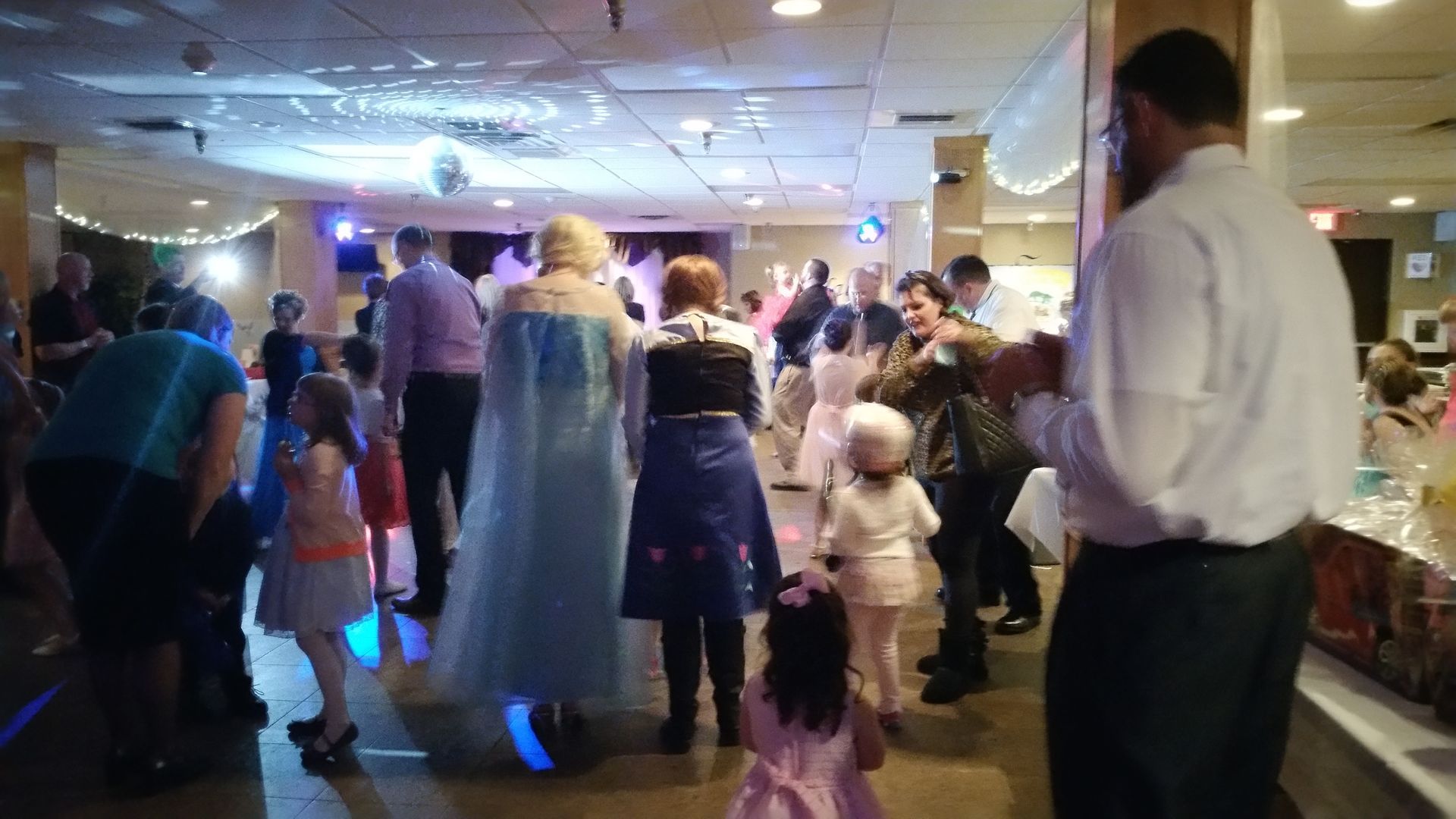 People dancing at a crowded indoor party with blue lights and festive decorations