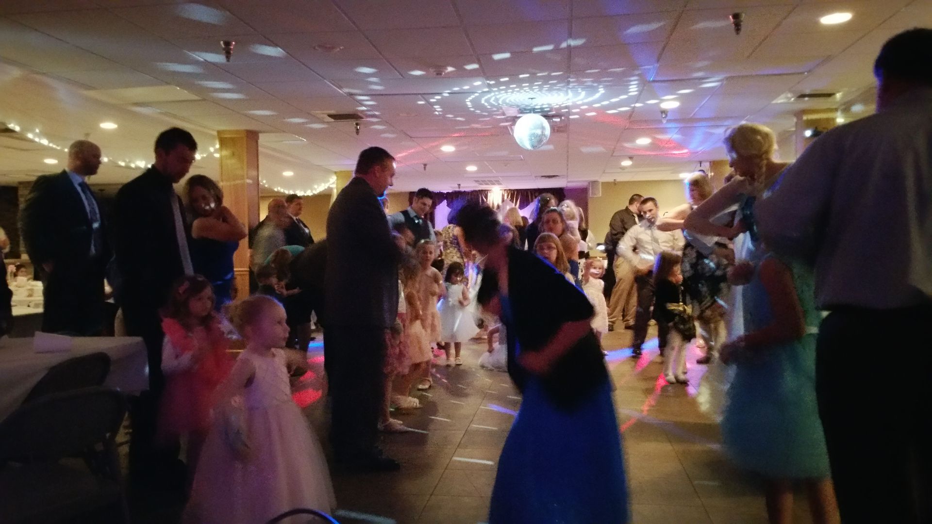 Guests dancing at a warmly lit indoor party with colorful lights and formal attire.