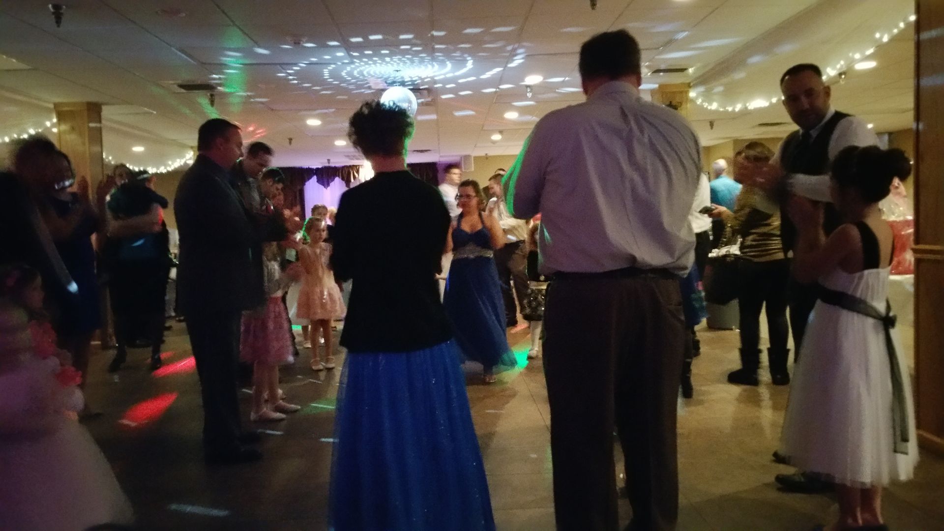 People dancing at a dimly lit indoor party with colorful lights on the floor and ceiling.