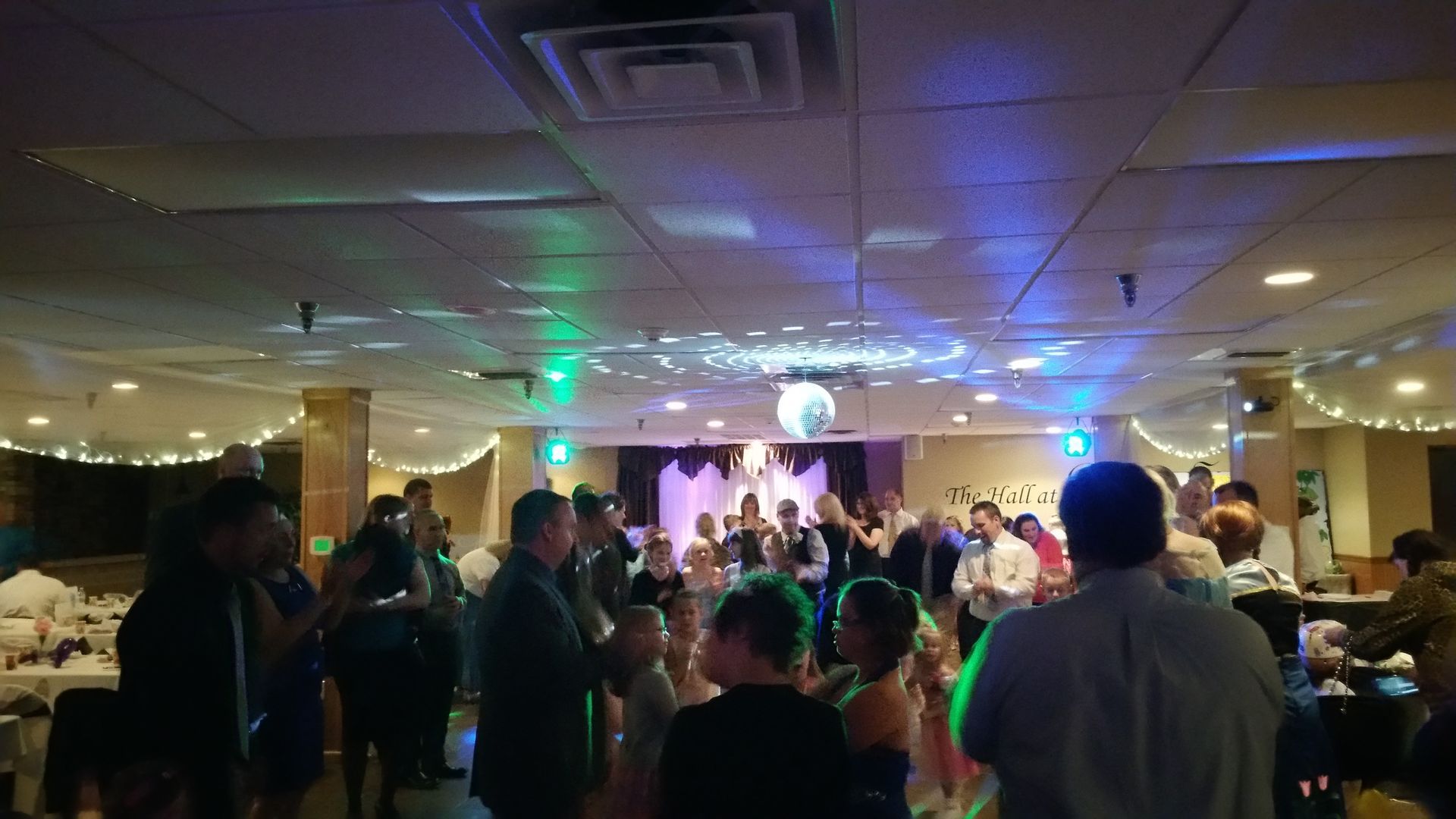 Crowded banquet hall with guests watching a lit stage and live performance under colorful lights