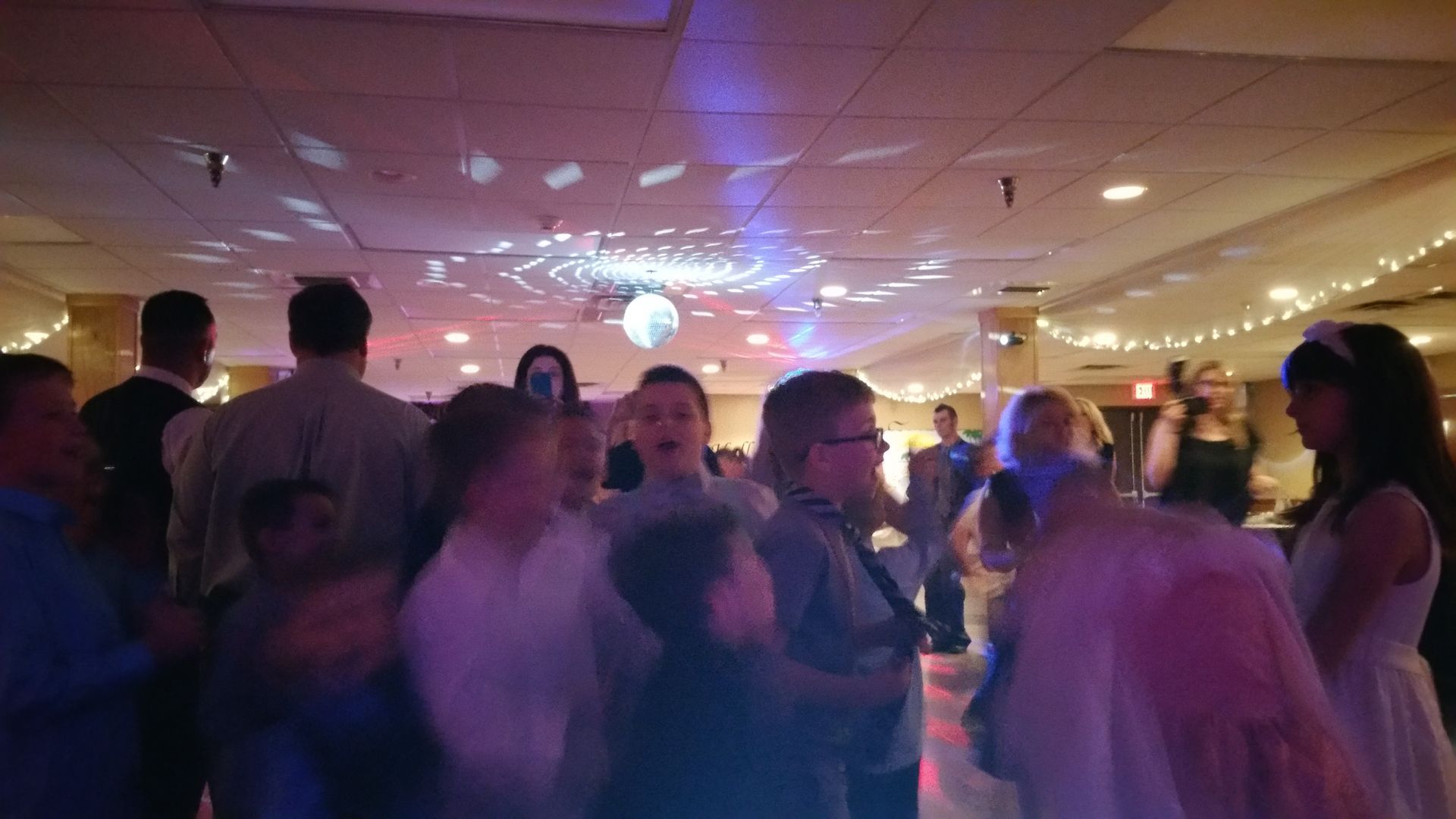 People dancing at a dimly lit party with string lights and a disco ball on the ceiling