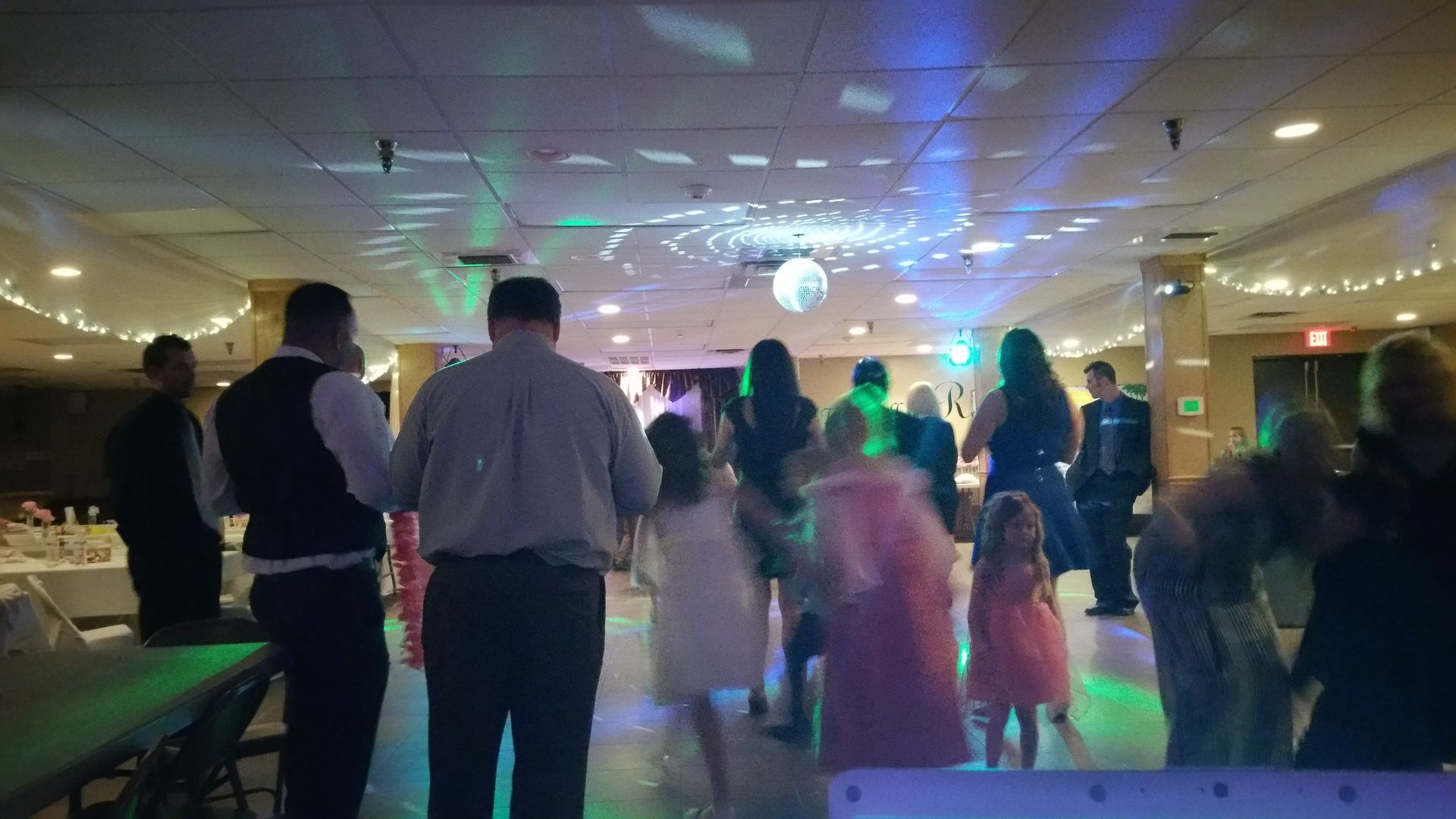 People dancing at a dimly lit party with colored lights and a disco ball.