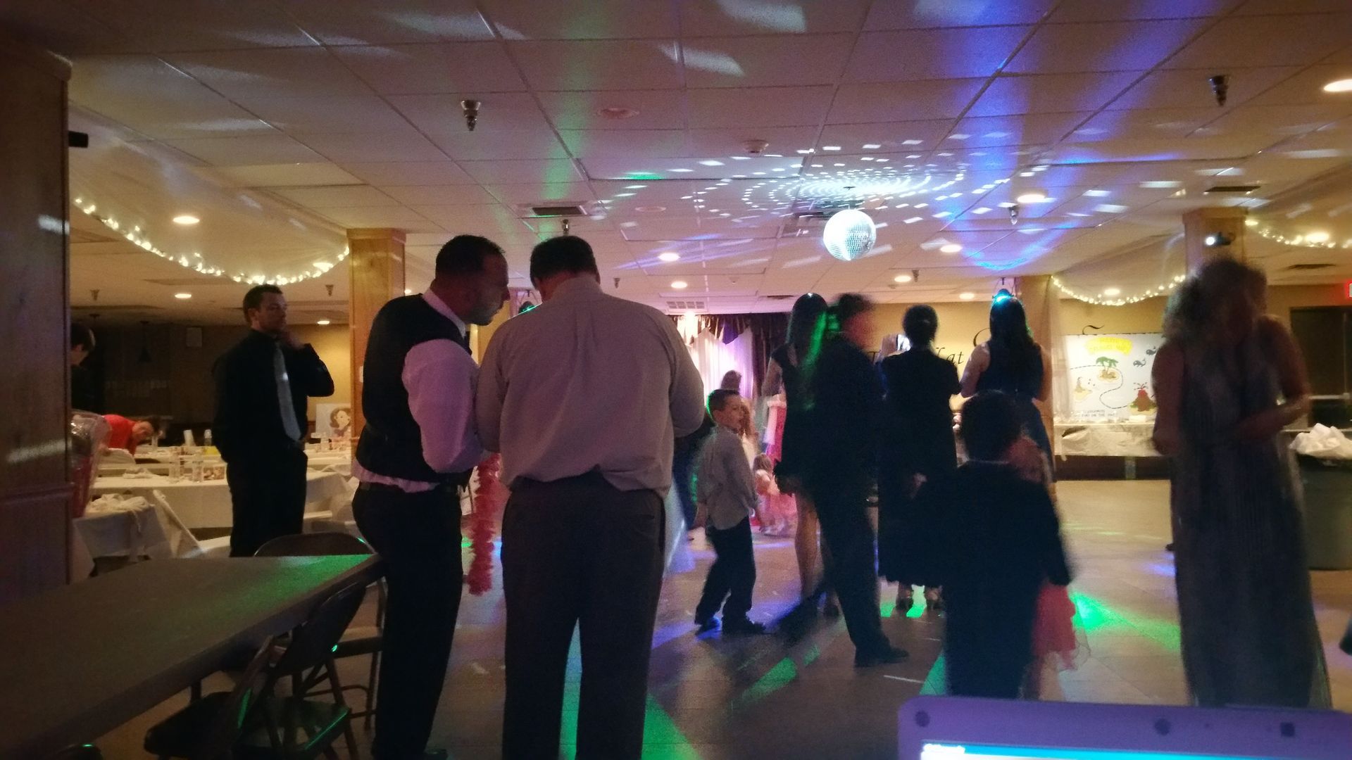 People mingling at a dimly lit party or reception with colorful ceiling lights and a dance floor