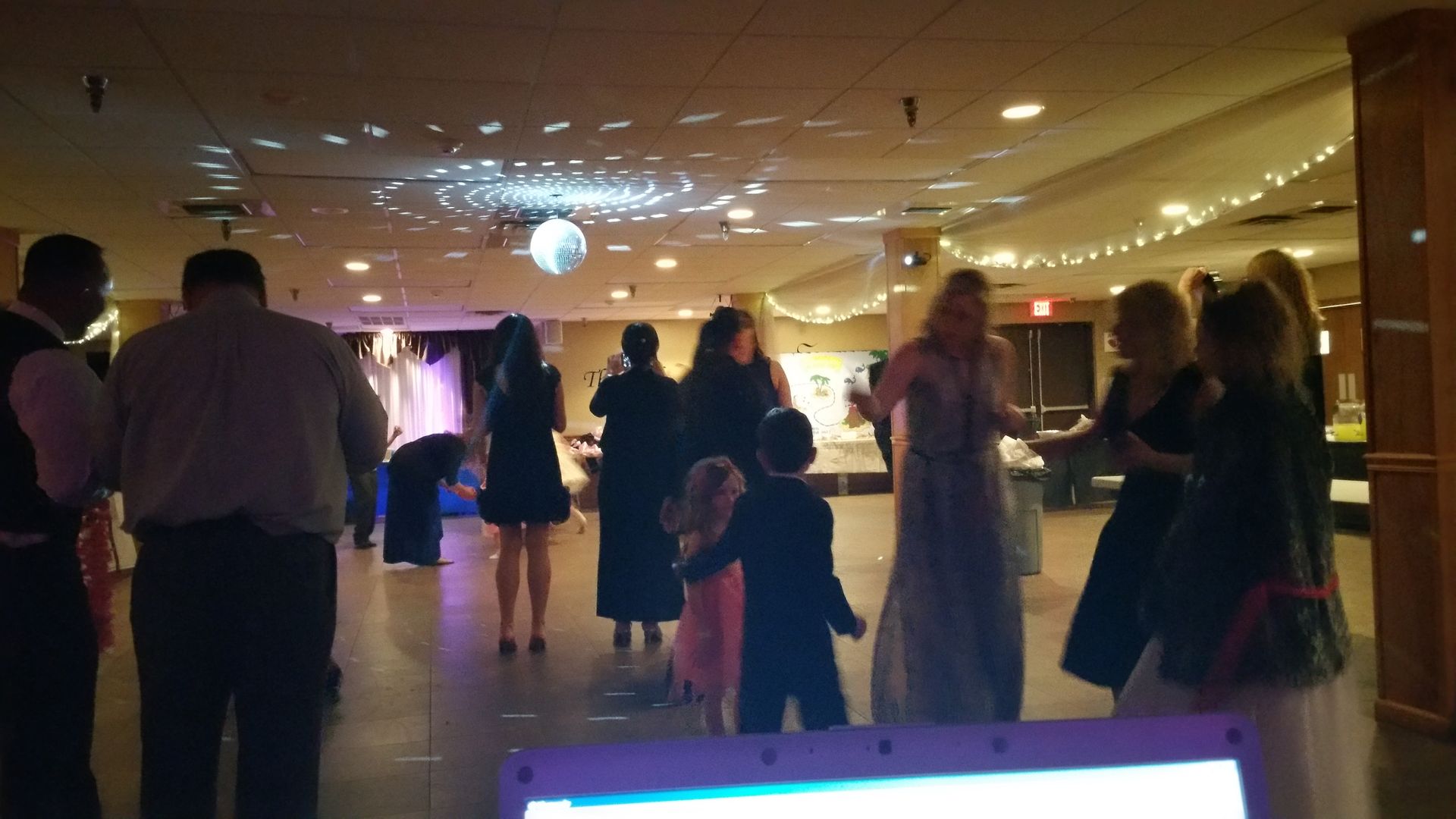 Guests mingling and dancing in a warmly lit banquet hall with a disco ball overhead