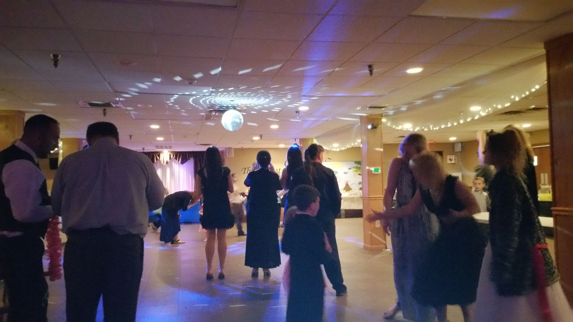 Guests dancing at a dimly lit indoor party with purple lighting and a disco ball.