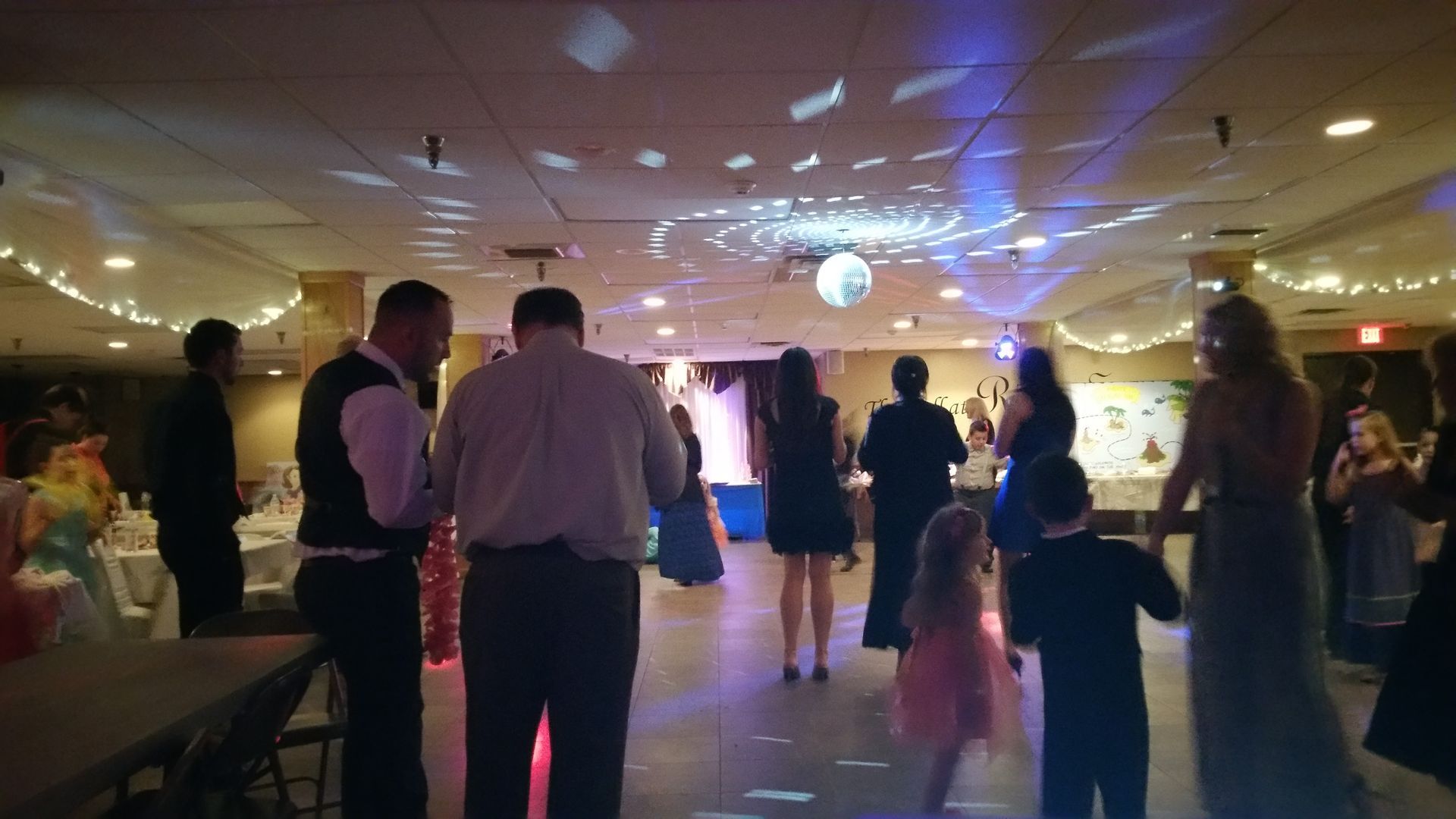 People dancing at a dimly lit party with colorful lights and a disco ball