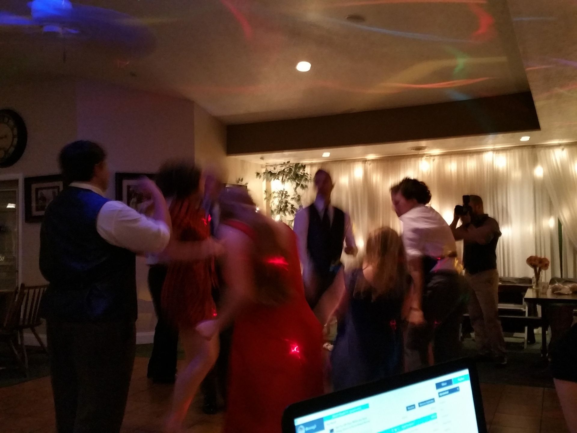 People dancing at a dimly lit party with colorful lights and a bright screen in the foreground