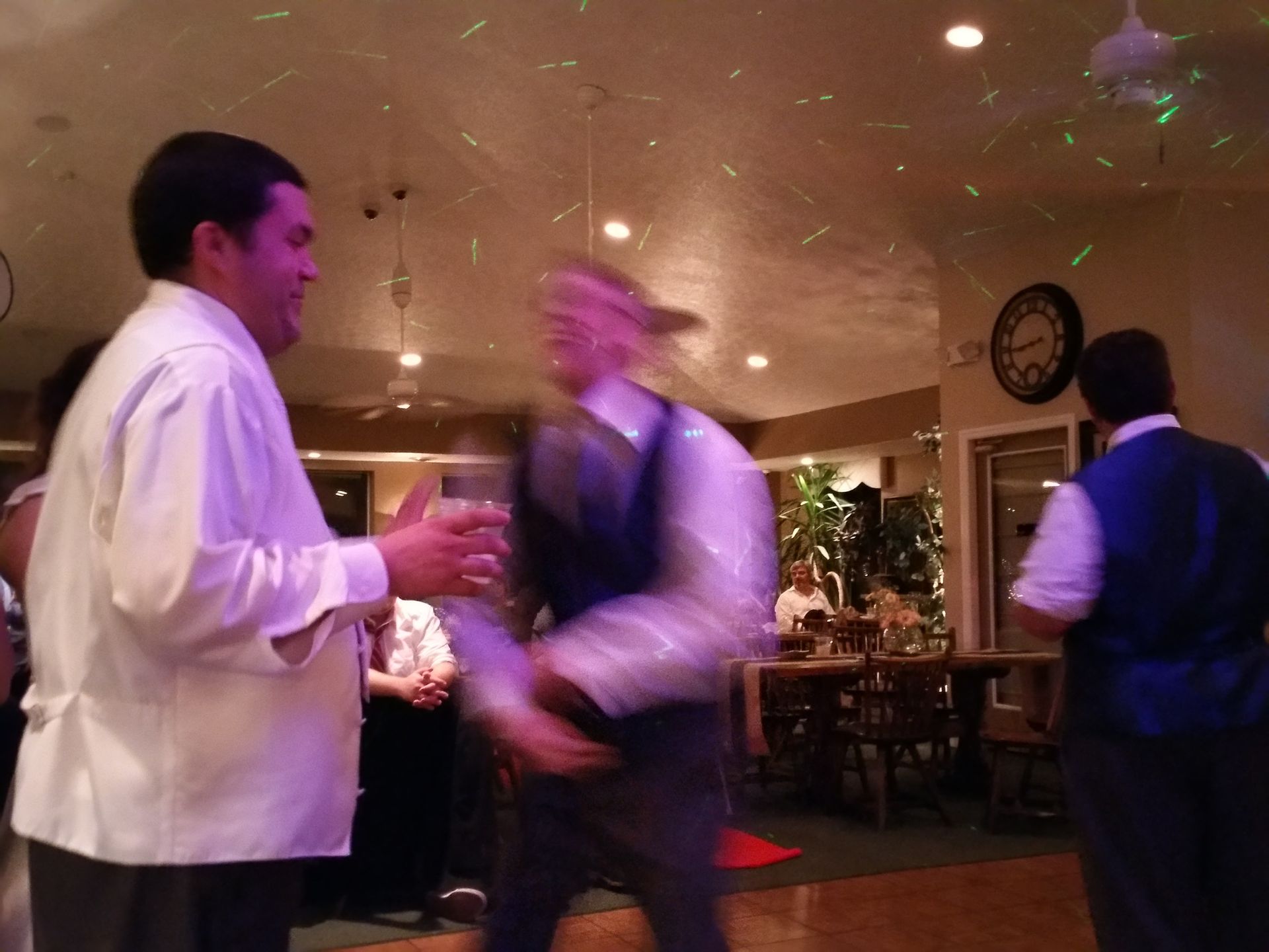 People conversing in a warmly lit restaurant, with one blurred figure moving in the foreground.