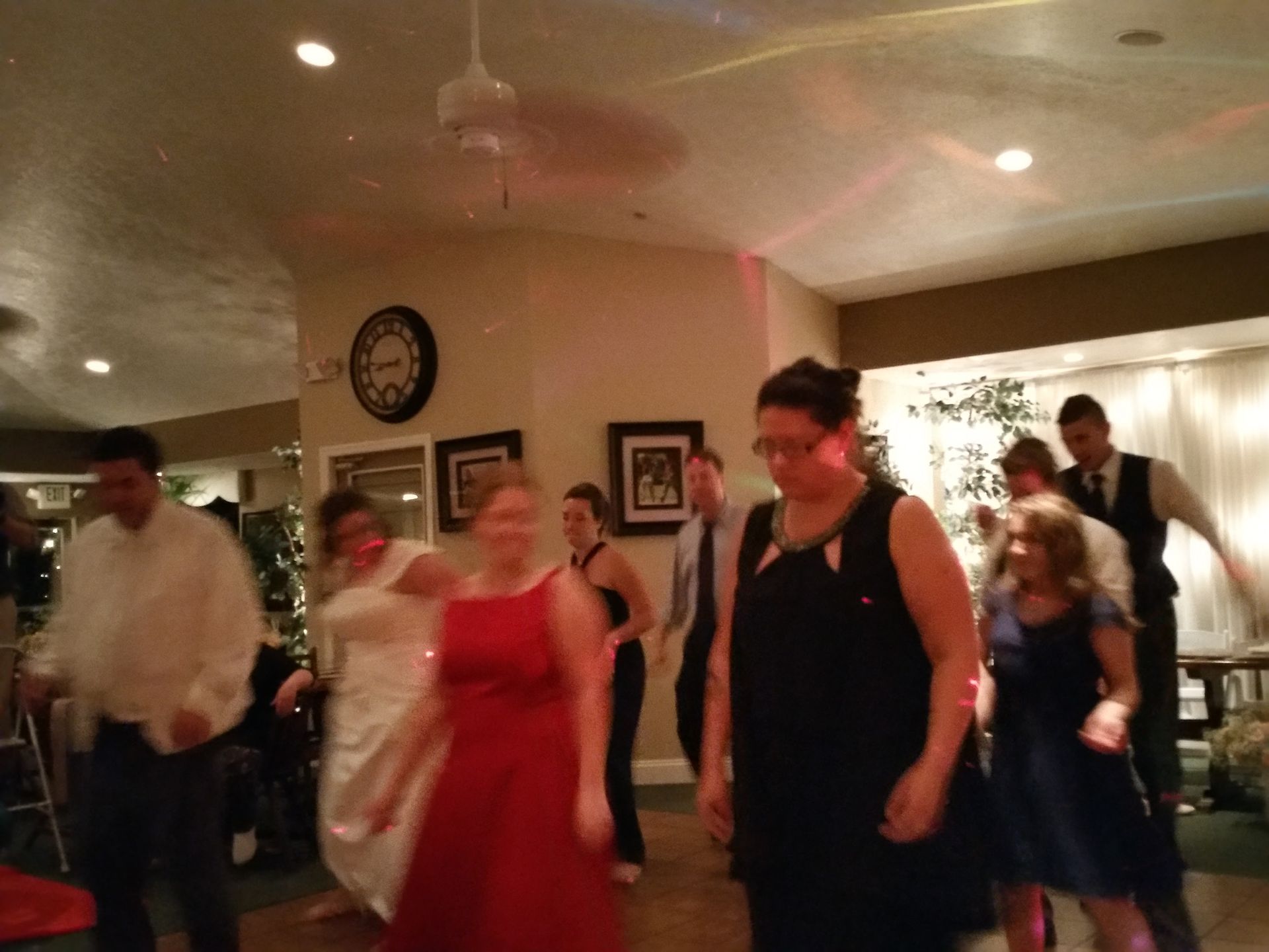 People dancing at an indoor party in formal attire, with a red dress centered in the foreground.