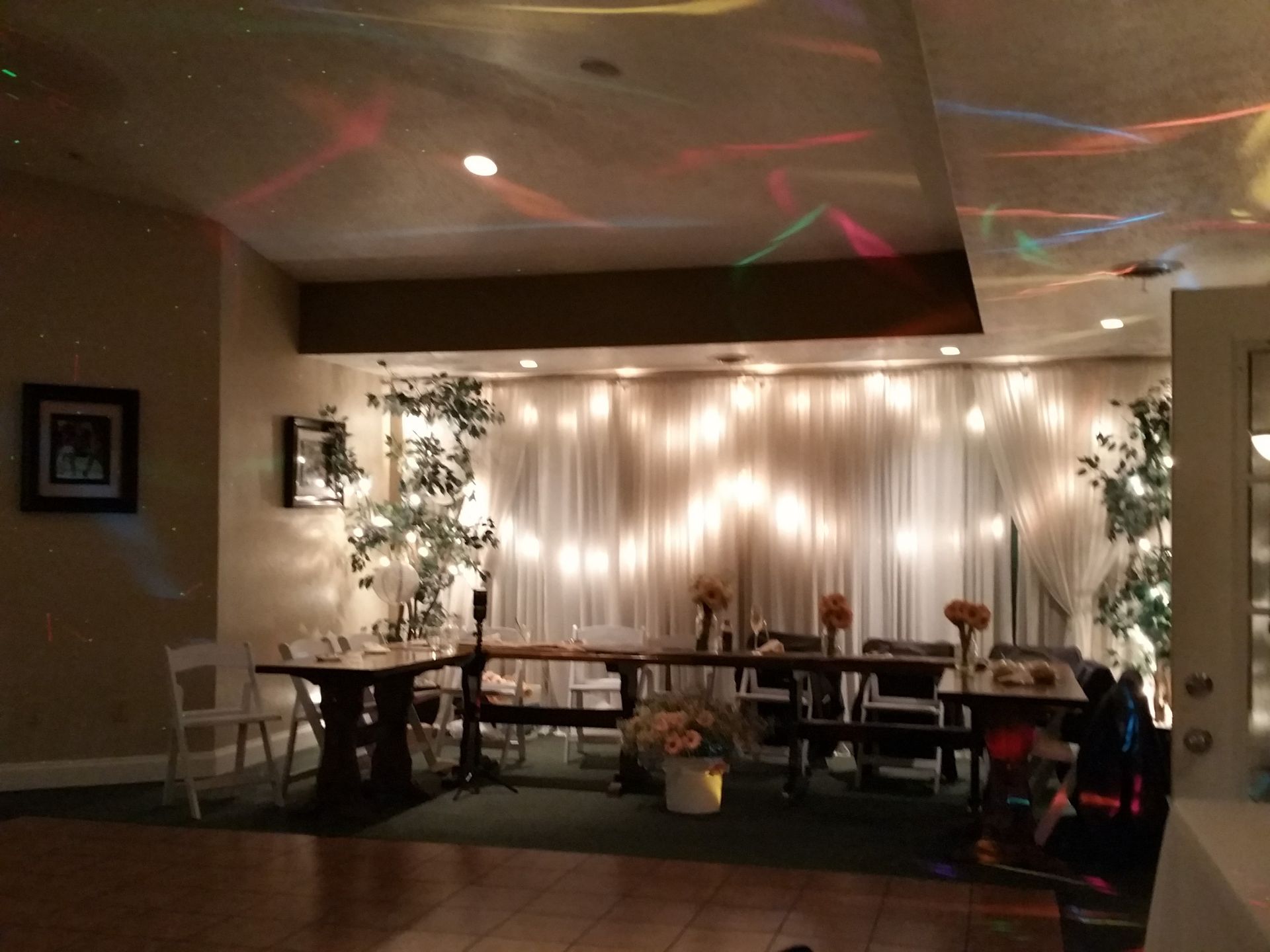 Dim banquet hall with a draped lighted backdrop, tables, and colorful ceiling lights