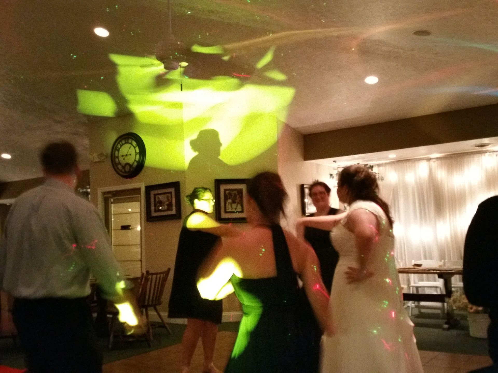 People dancing at a dimly lit indoor party with green light projections on the wall