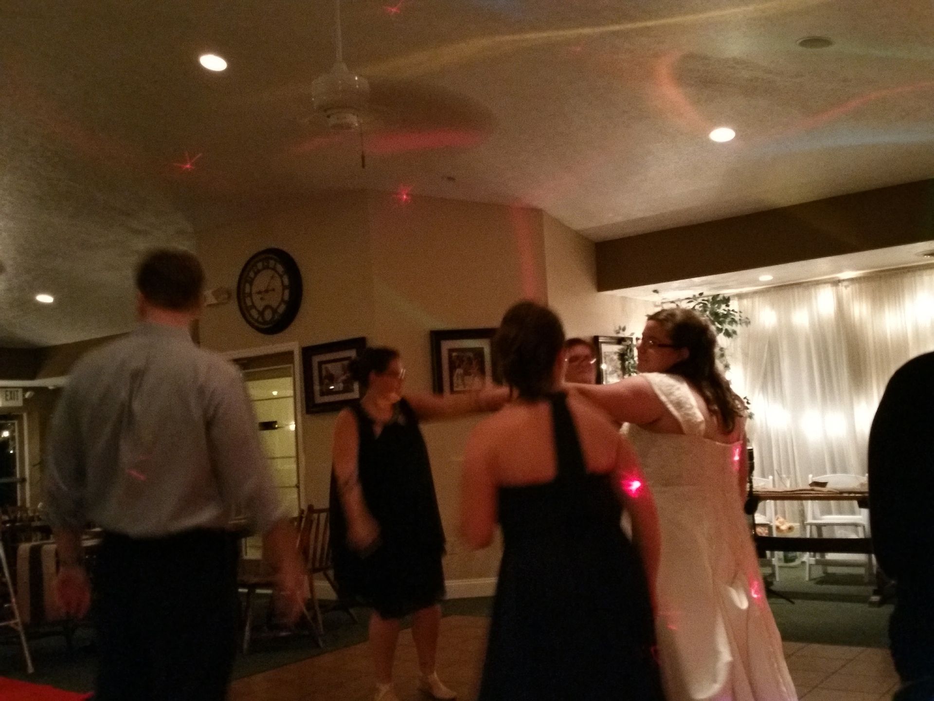 Guests dancing at a dimly lit indoor party, with red light reflections and string lights in the background