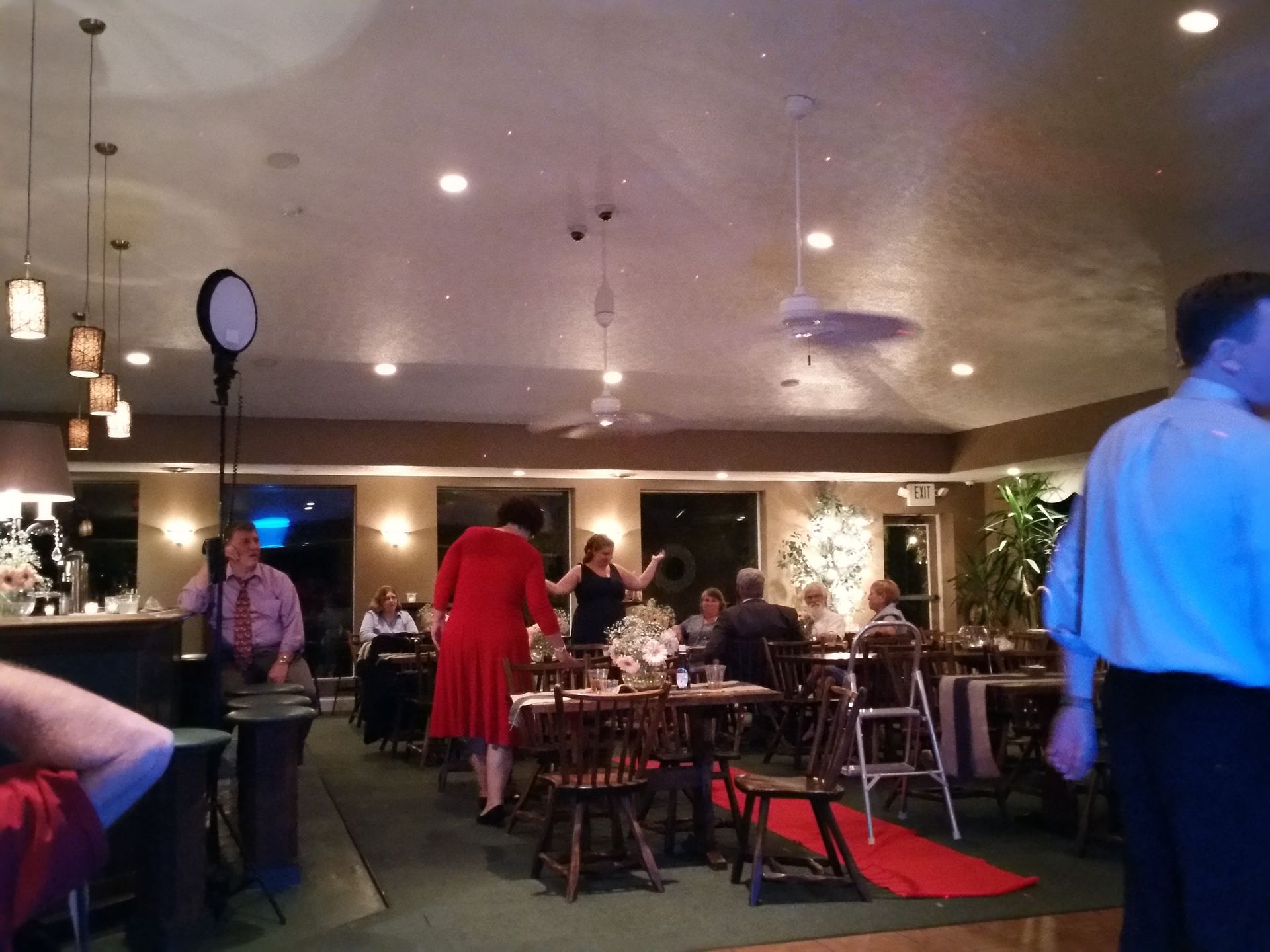 Indoor bar with people mingling around tables, red carpet, and warm overhead lighting.