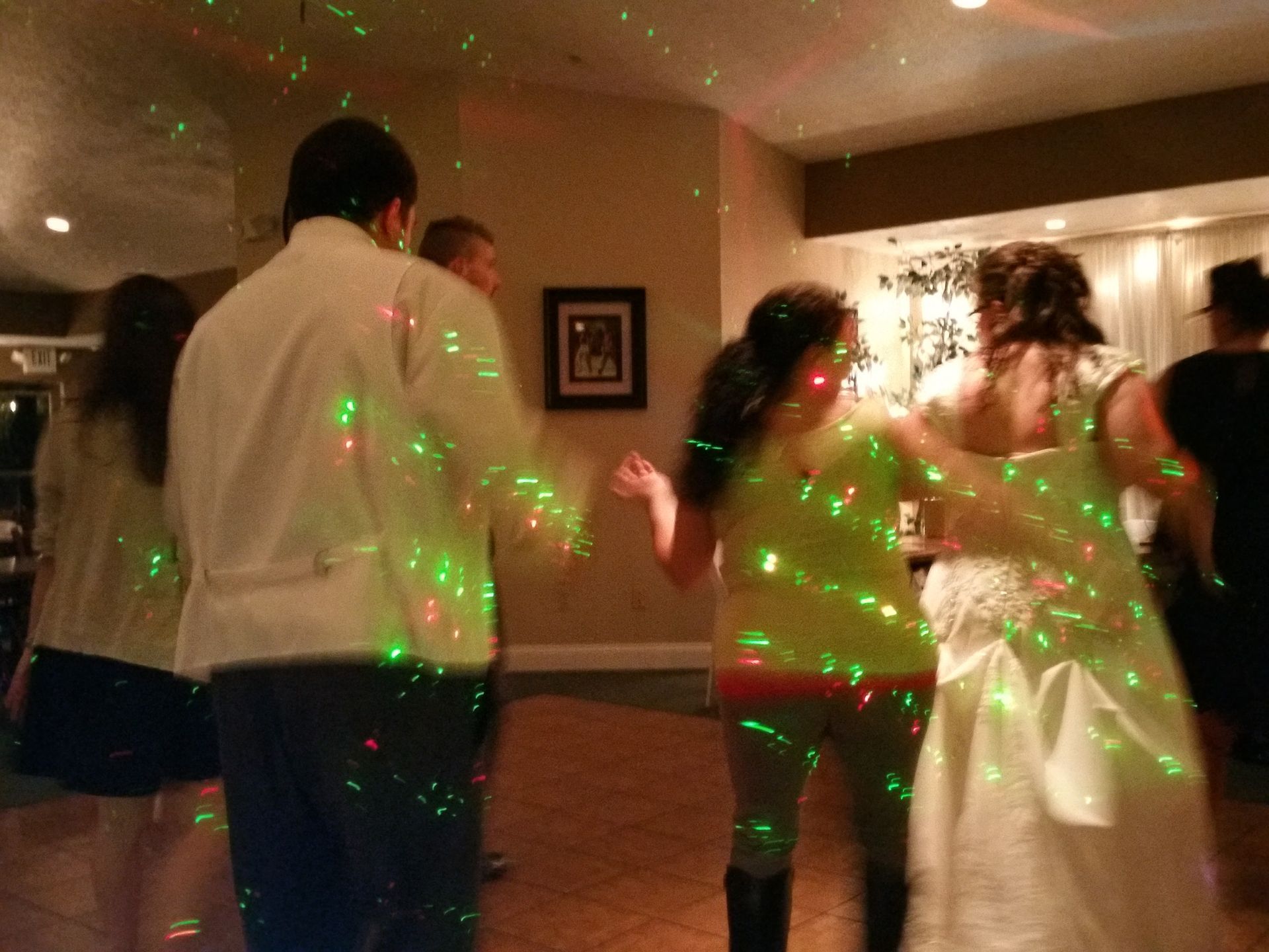 People dancing in a banquet hall under green laser lights, with a bride in a white gown.