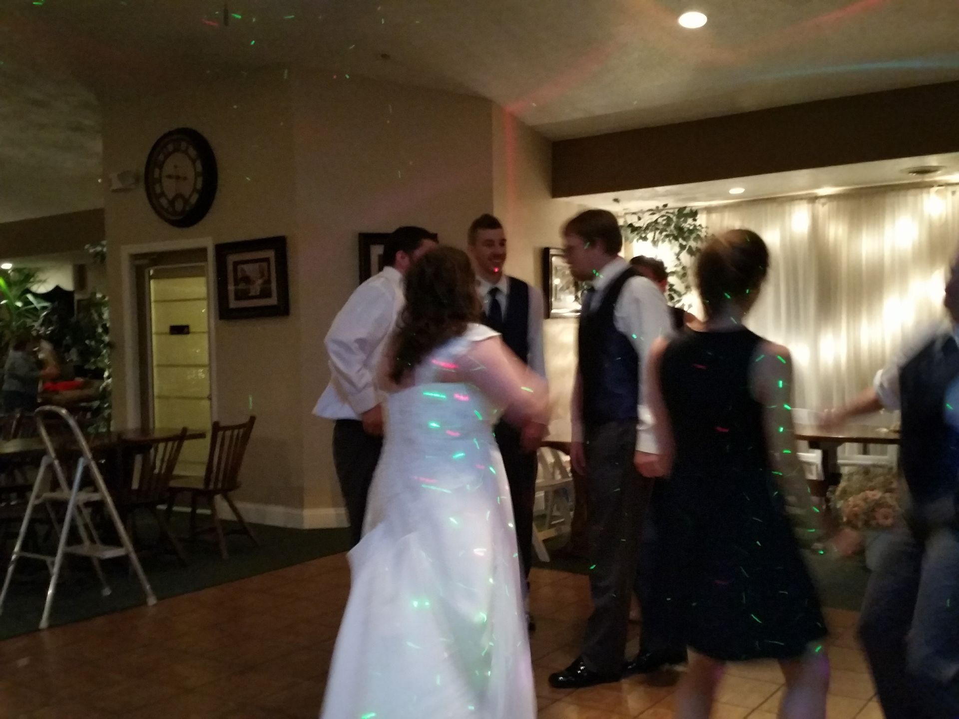 People dancing at a small indoor party with warm lights and tables in the background
