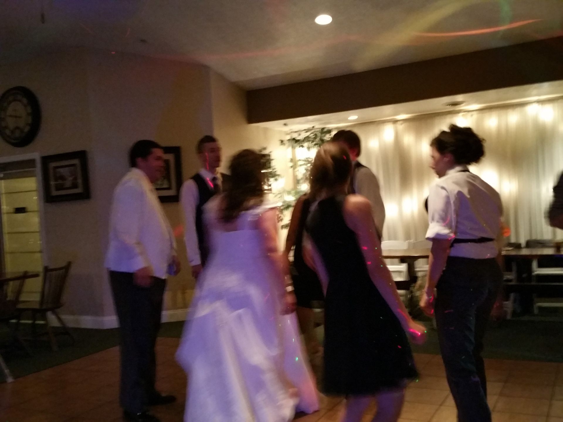 People socializing and dancing at a dimly lit indoor reception with string lights.
