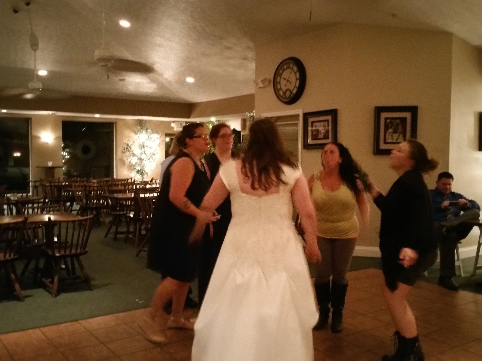 People dancing at an indoor reception, with a bride in a white dress at the center.