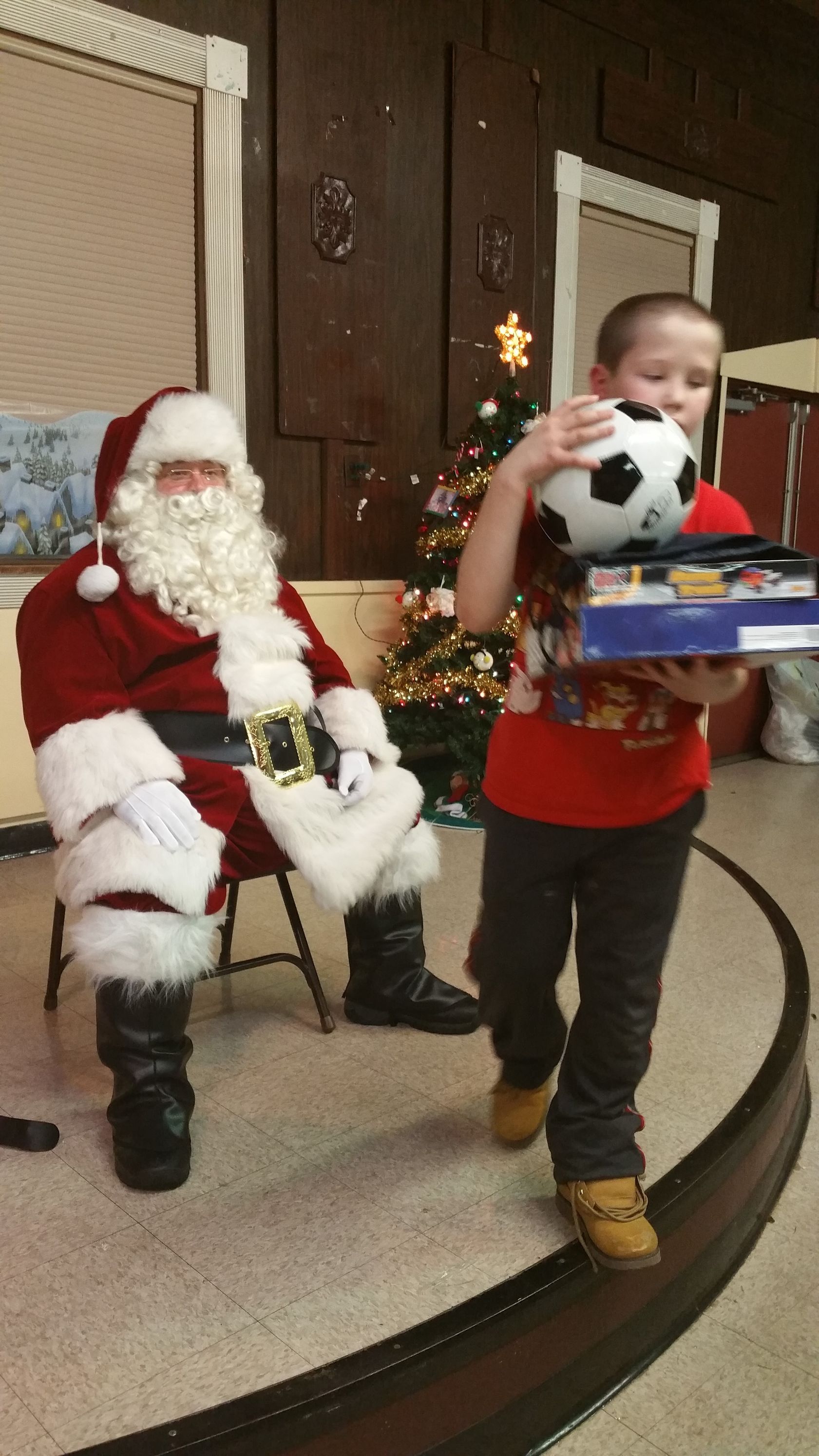 Child holding a wrapped gift and a soccer ball beside Santa in a holiday display