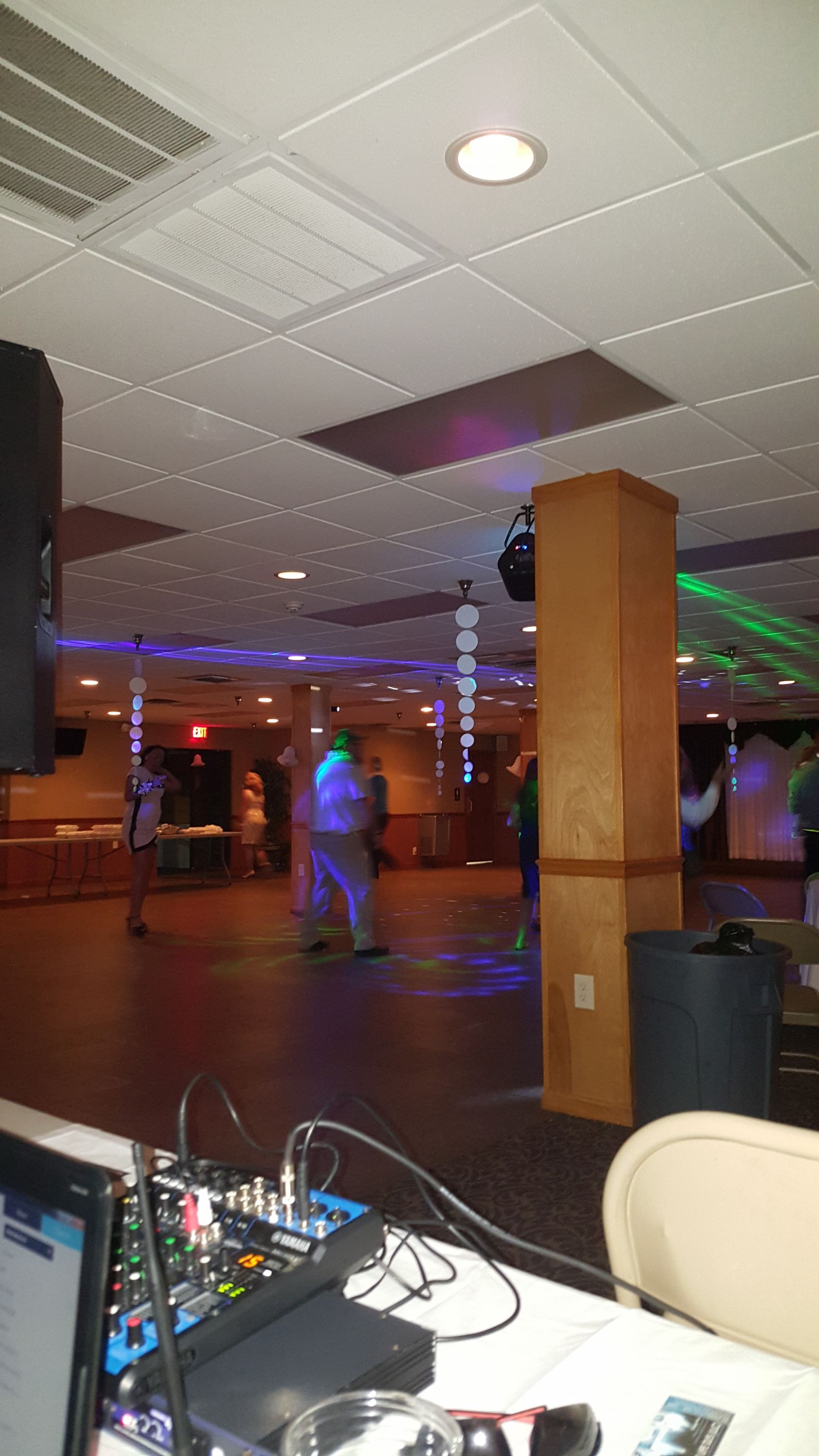 Dimly lit dance hall with disco lights, wooden columns, and a DJ booth in the foreground