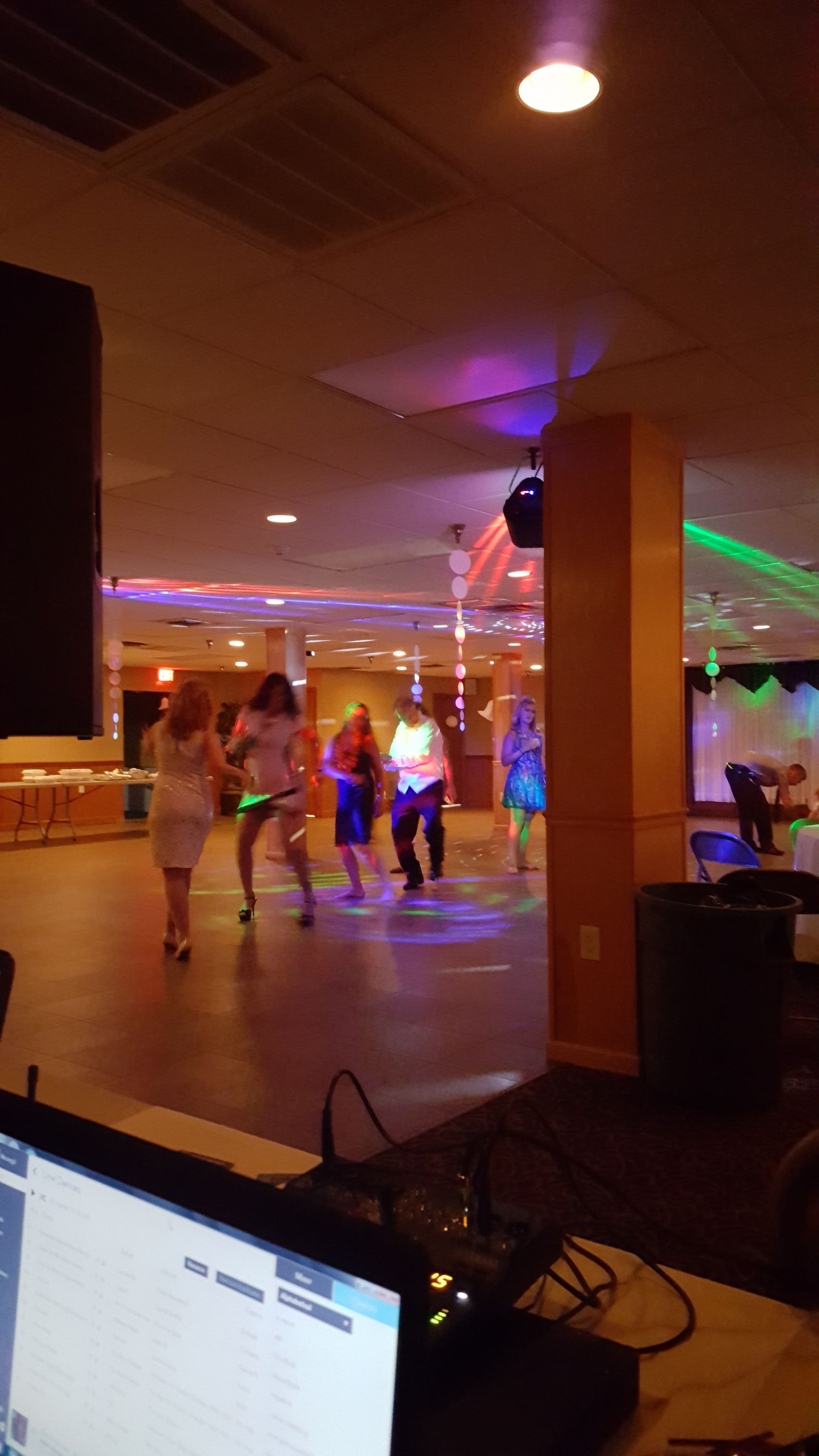 People dancing in a dimly lit lounge with colorful floor lights and a TV screen in the foreground.