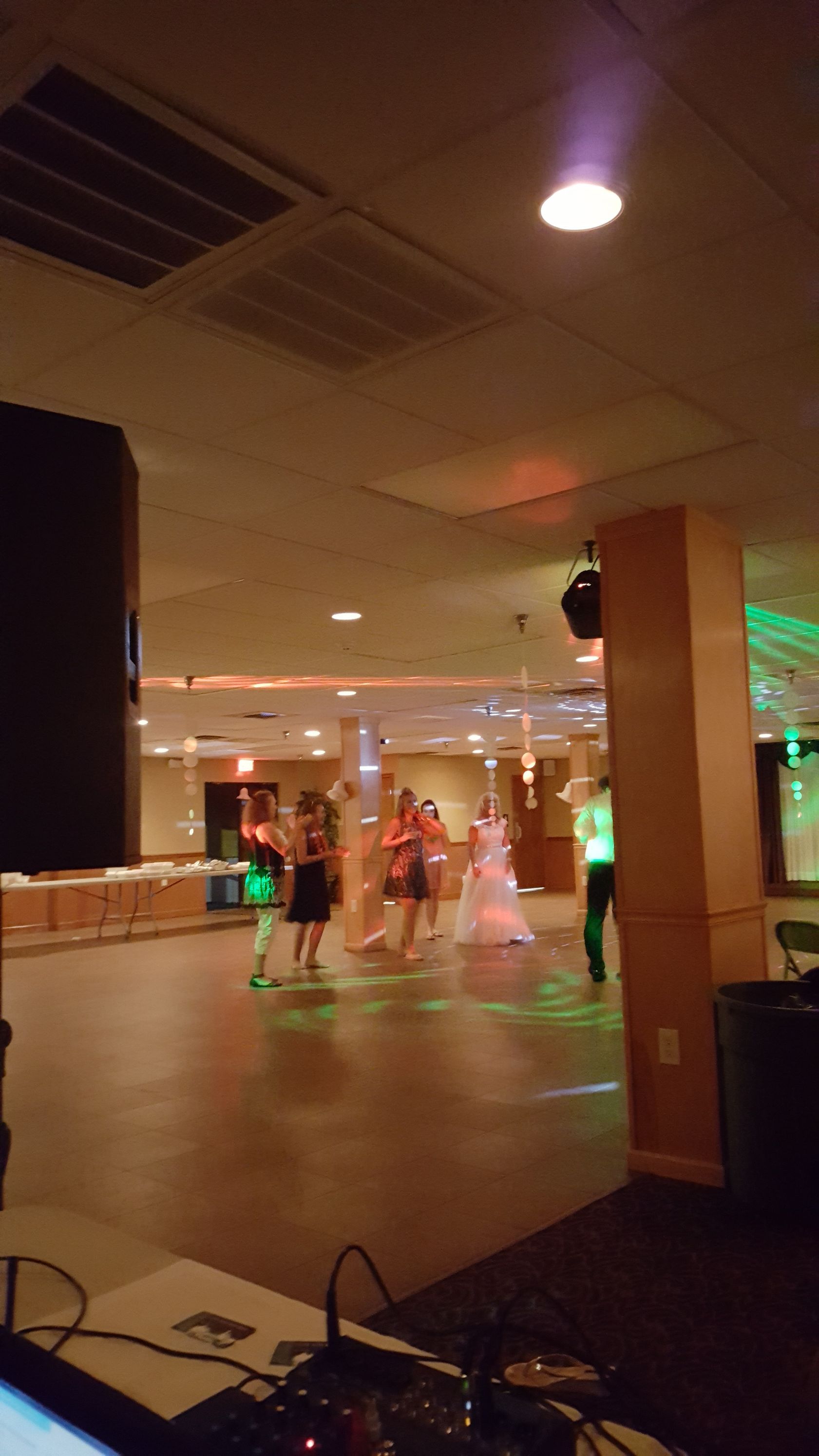 People dancing in a dimly lit hall with colorful lights and a wooden floor.