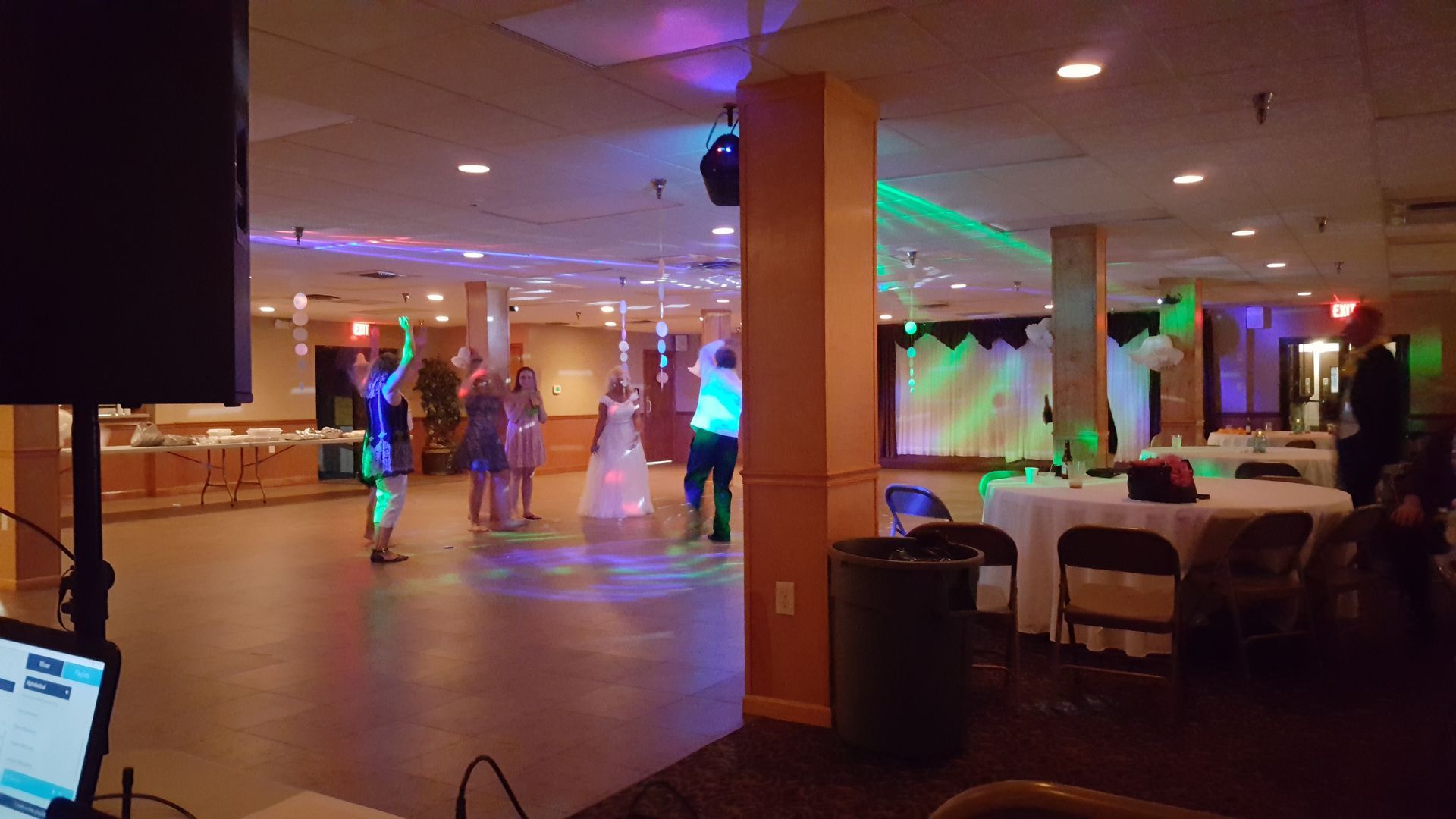 Dimly lit banquet hall with people dancing, tables, and colored stage lights