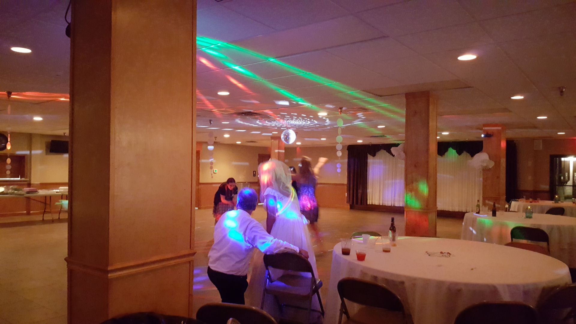 People seated at tables in a banquet hall, with colorful laser lights across the ceiling.